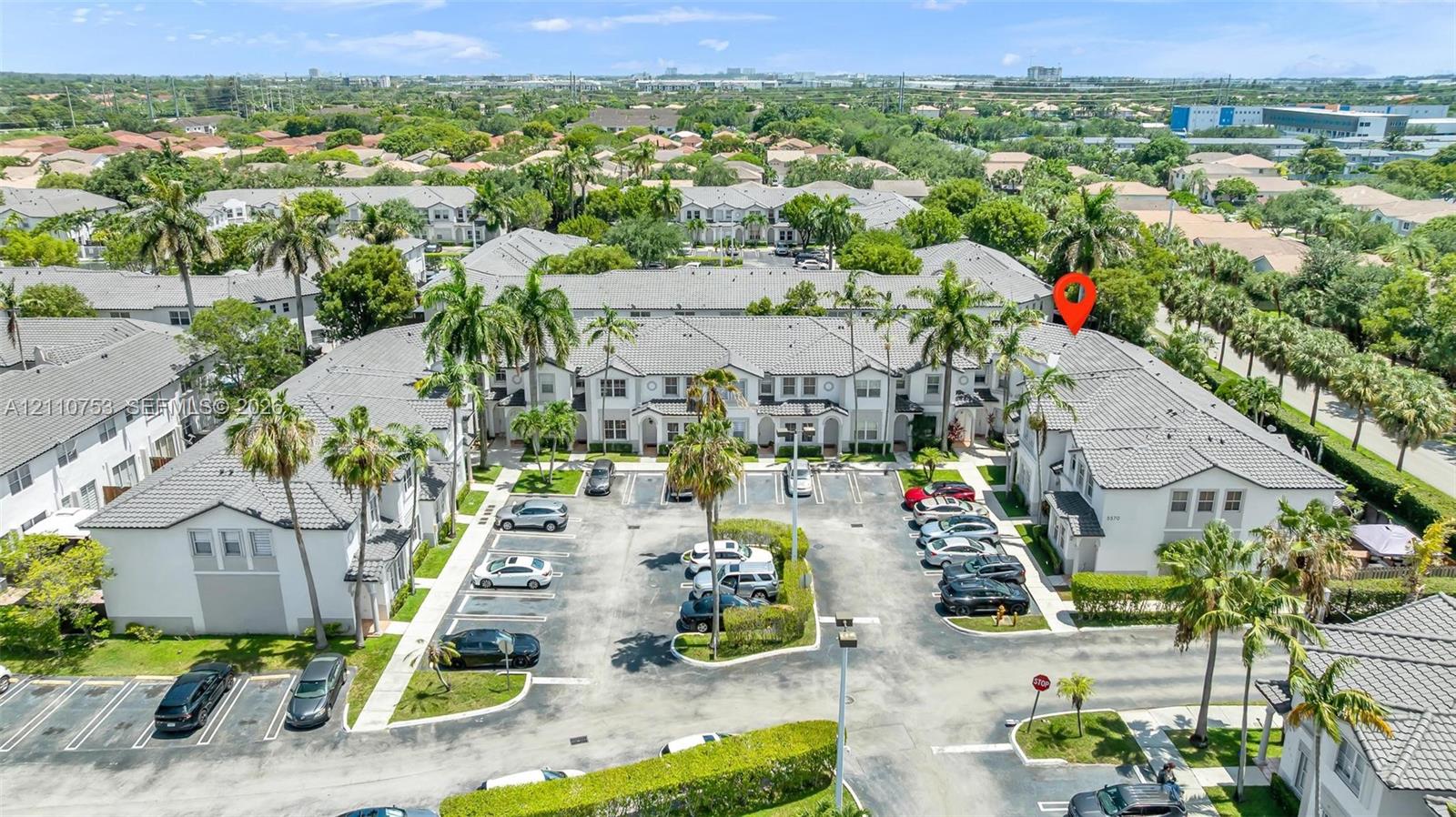 Aerial perspective of a multi-unit residential complex featuring tile roofing, stucco exterior finishes, integrated parking areas, and mature palm landscaping