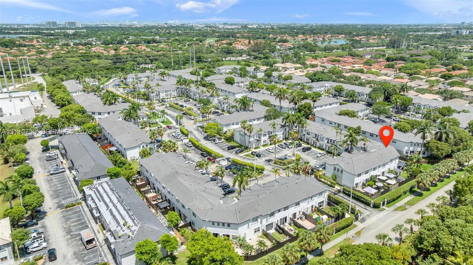 Aerial perspective of a multi-unit residential complex featuring gray pitched roofs, paved parking areas, and mature palm tree landscaping