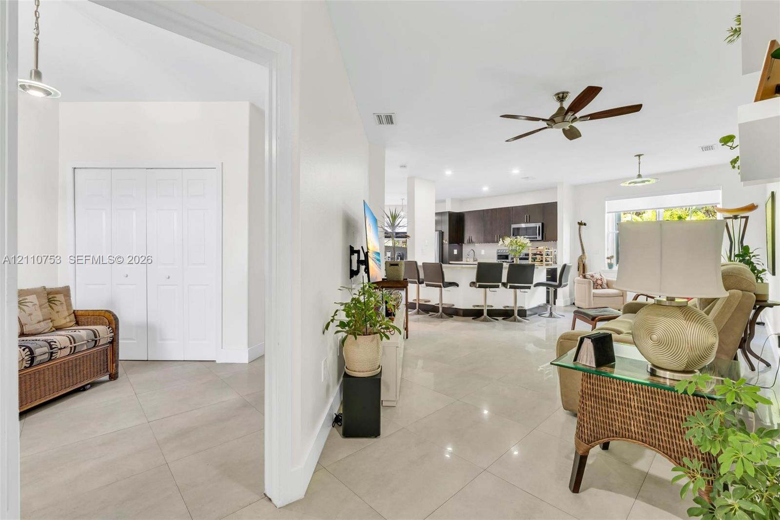 Open-concept interior featuring large-format tile flooring, a chef's kitchen with dark cabinetry, a curved island with integrated seating, recessed lighting, and a ceiling fan