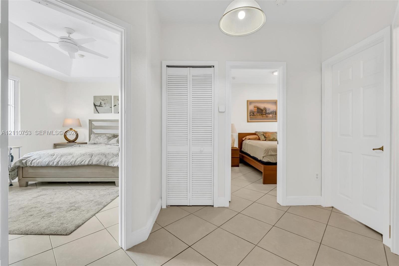 Neutral-toned tile flooring, white six-panel interior doors, and built-in closet with white louvered doors