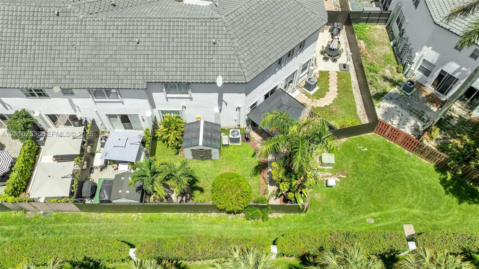 Aerial perspective featuring a private backyard with mature landscaping, a paved patio area, and perimeter fencing