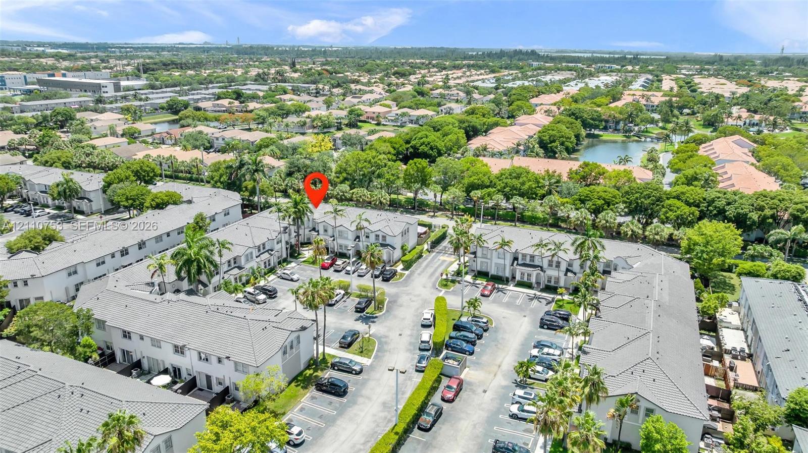 Aerial perspective of multi-family community featuring paved surface parking, mature palm trees, and manicured landscaping