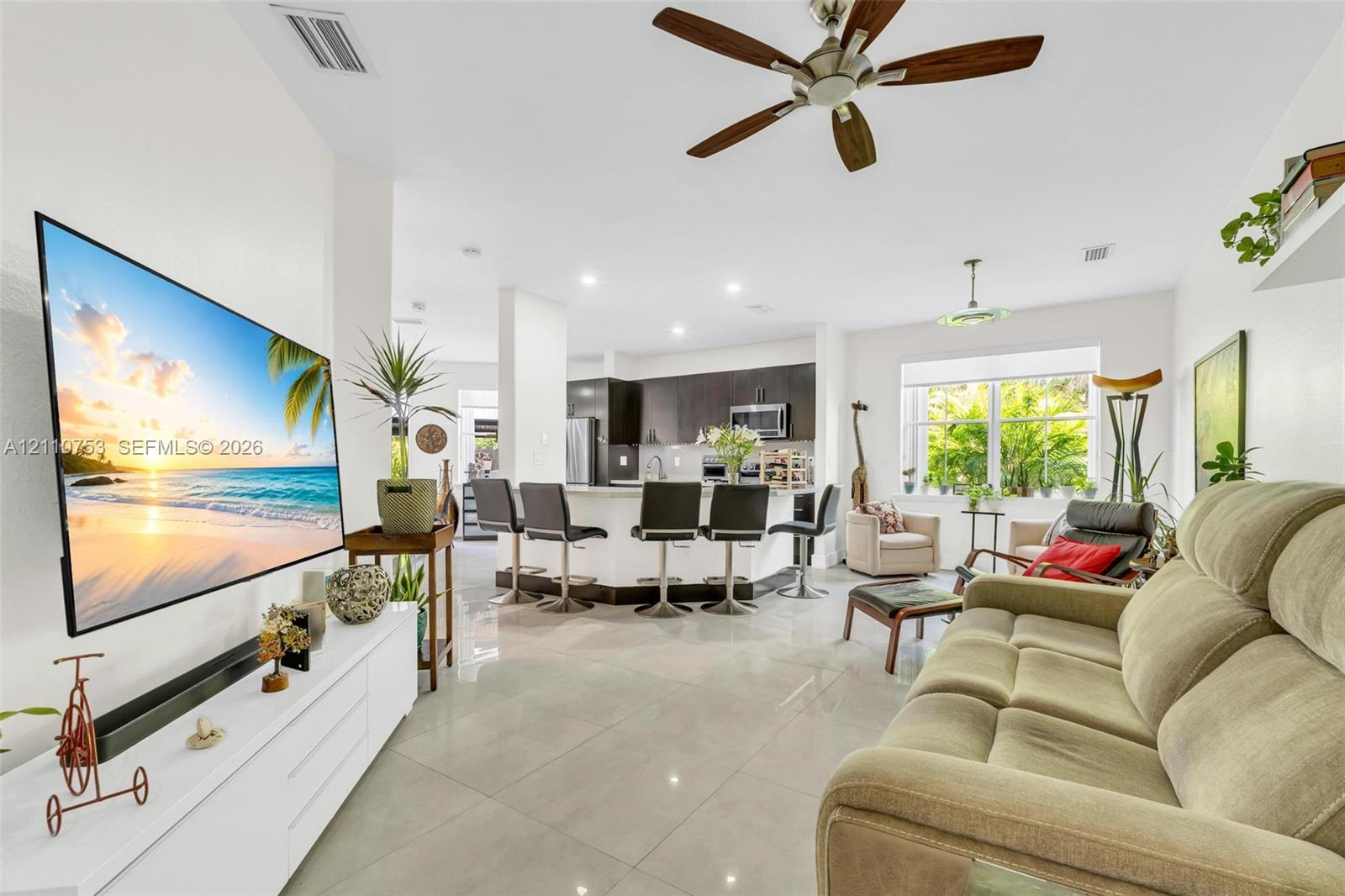 Open-concept interior featuring large-format tile flooring, recessed ceiling lighting, a multi-blade ceiling fan, and a kitchen island with built-in cabinetry