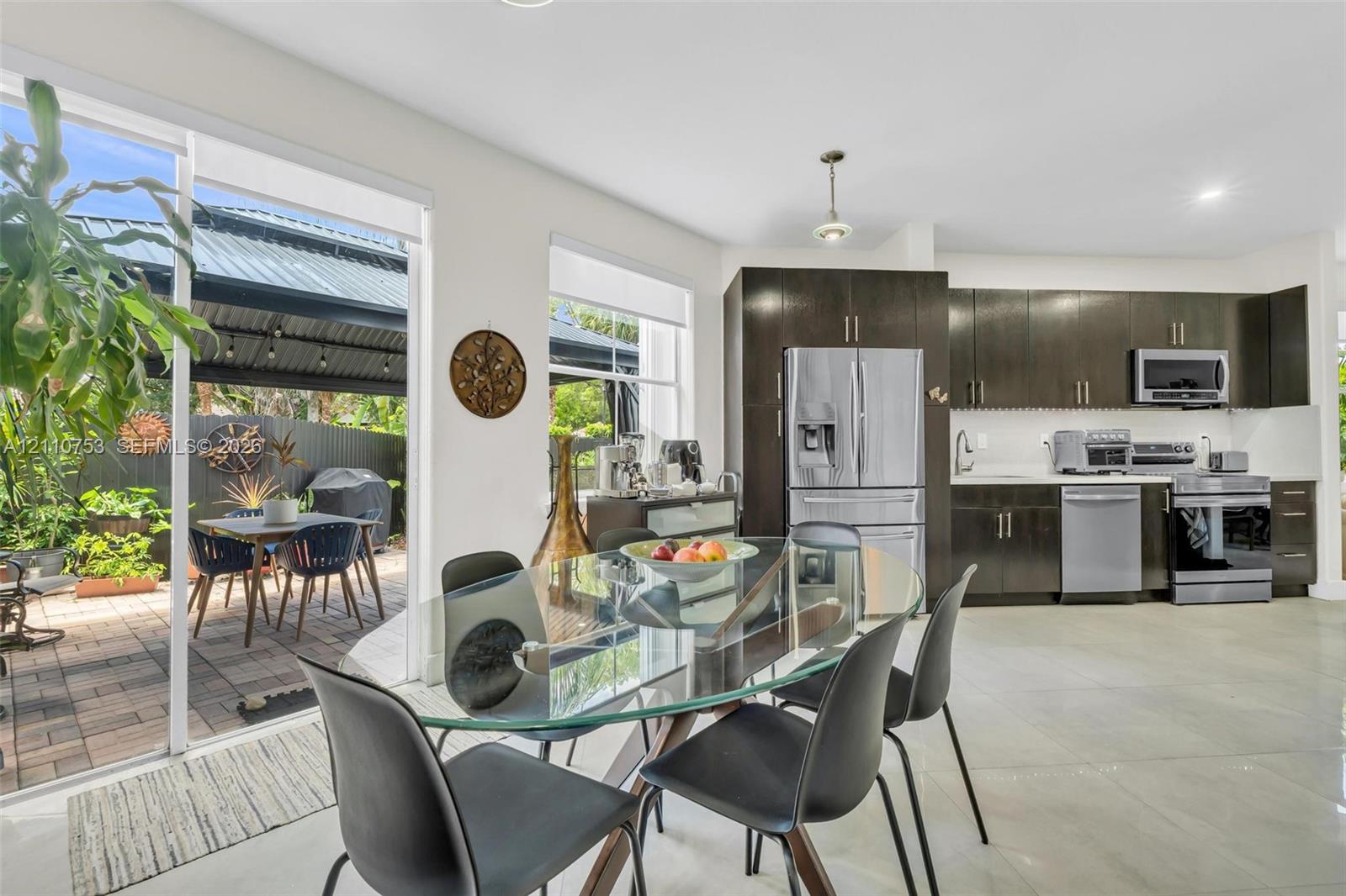Kitchen featuring dark wood-finish cabinetry, stainless steel appliances, and large-format tile flooring, complete with a sliding glass door providing access to the exterior patio