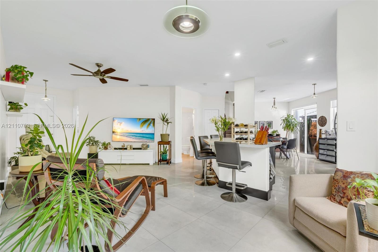 Open-concept interior featuring large-format tile flooring, recessed lighting, and a kitchen island with a breakfast bar
