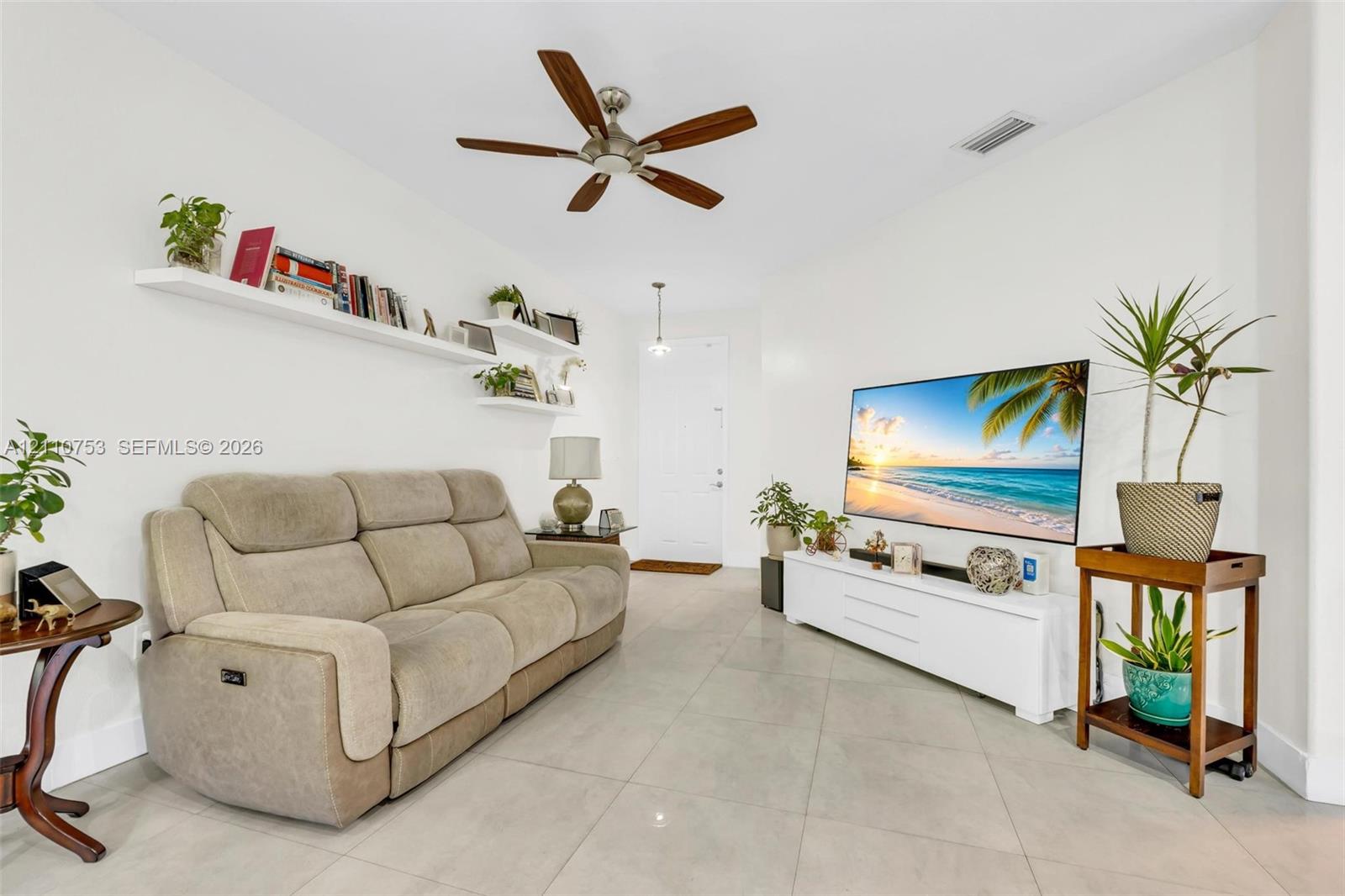 Large-format tile flooring, multi-blade ceiling fan, and wall-mounted floating shelving