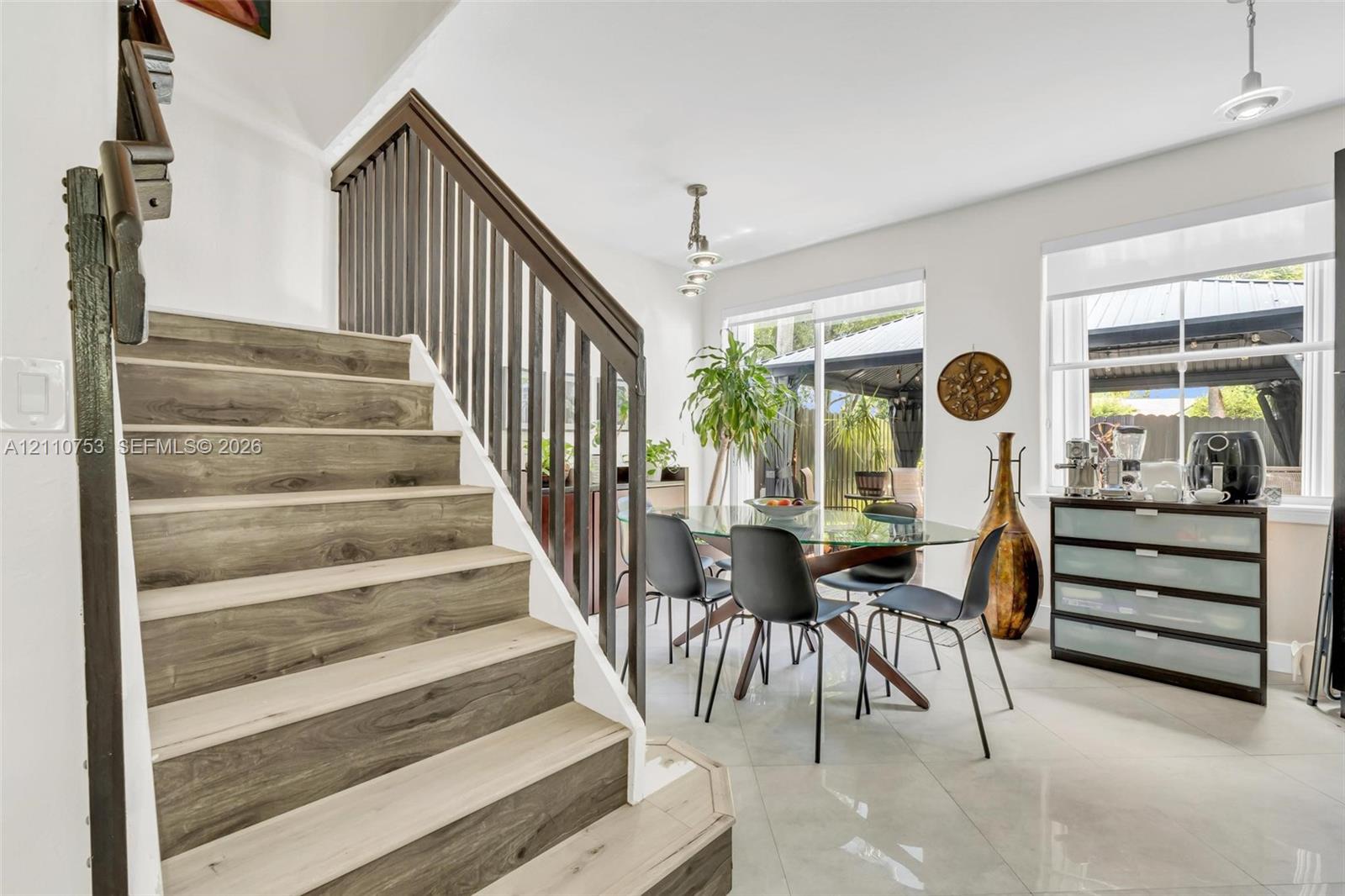 Staircase featuring wood-finish treads and dark vertical metal balusters, large-format tile flooring, multi-pane windows, and modern pendant lighting