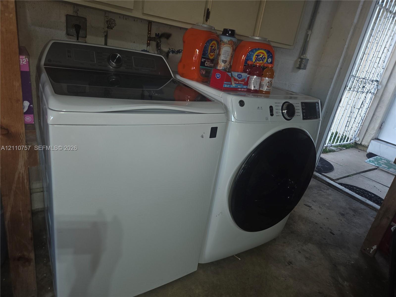 White top-load washer and front-load dryer featuring glass-top lids, digital control panels, and dark-finish circular door trim