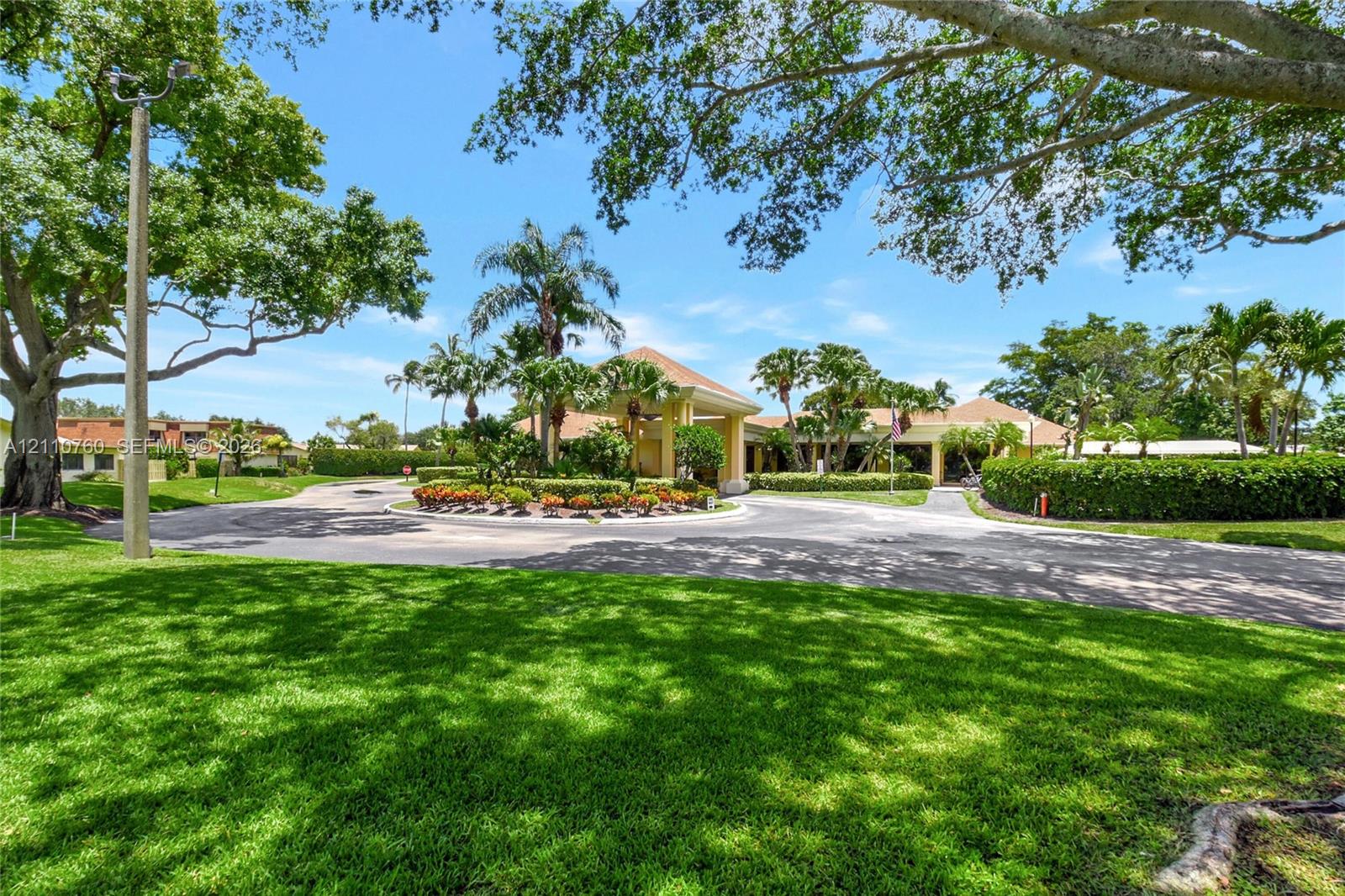 Circular driveway featuring mature tropical landscaping, a covered porte-cochre, and manicured lawns