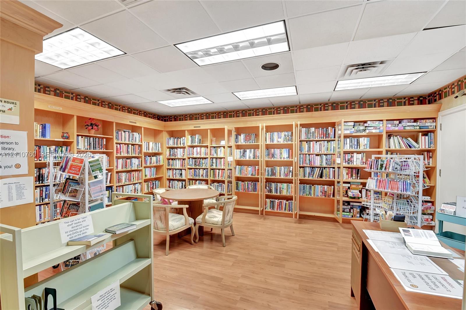 Expansive library space featuring full-height built-in wood shelving, drop ceiling with integrated recessed lighting, and wood-finish flooring