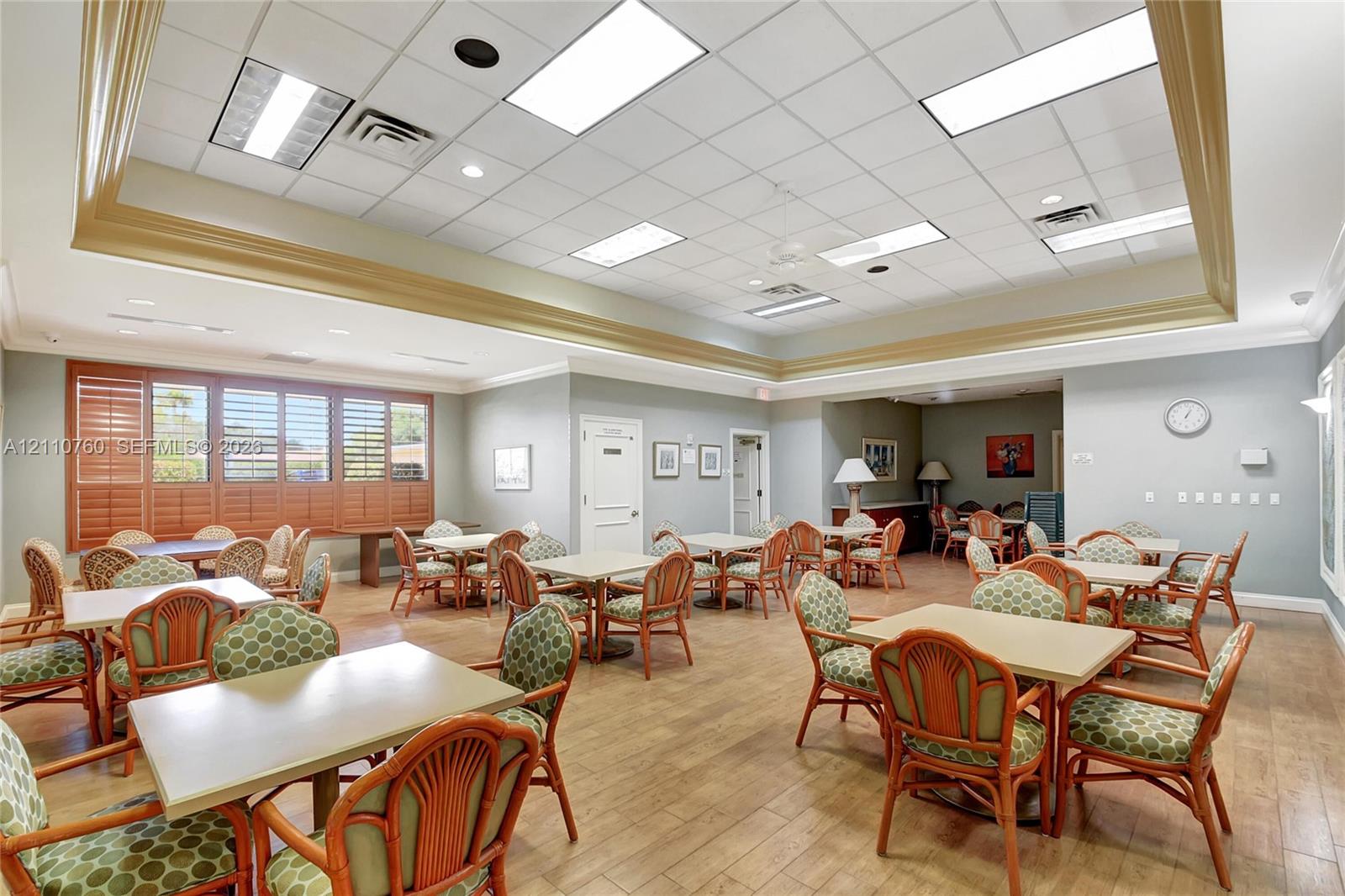 Spacious interior featuring wood-finish flooring, a recessed tray ceiling, drop-tile ceiling panels, and plantation shutters