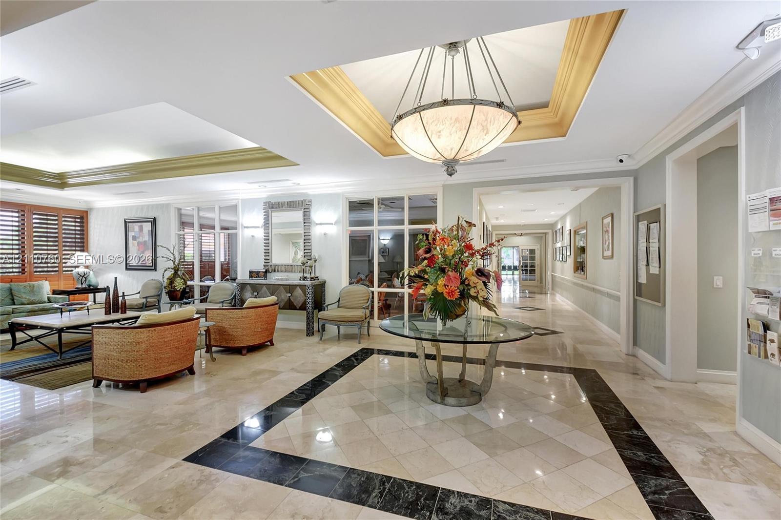Polished stone flooring with decorative geometric inlay, recessed tray ceiling, and grand pendant lighting fixture