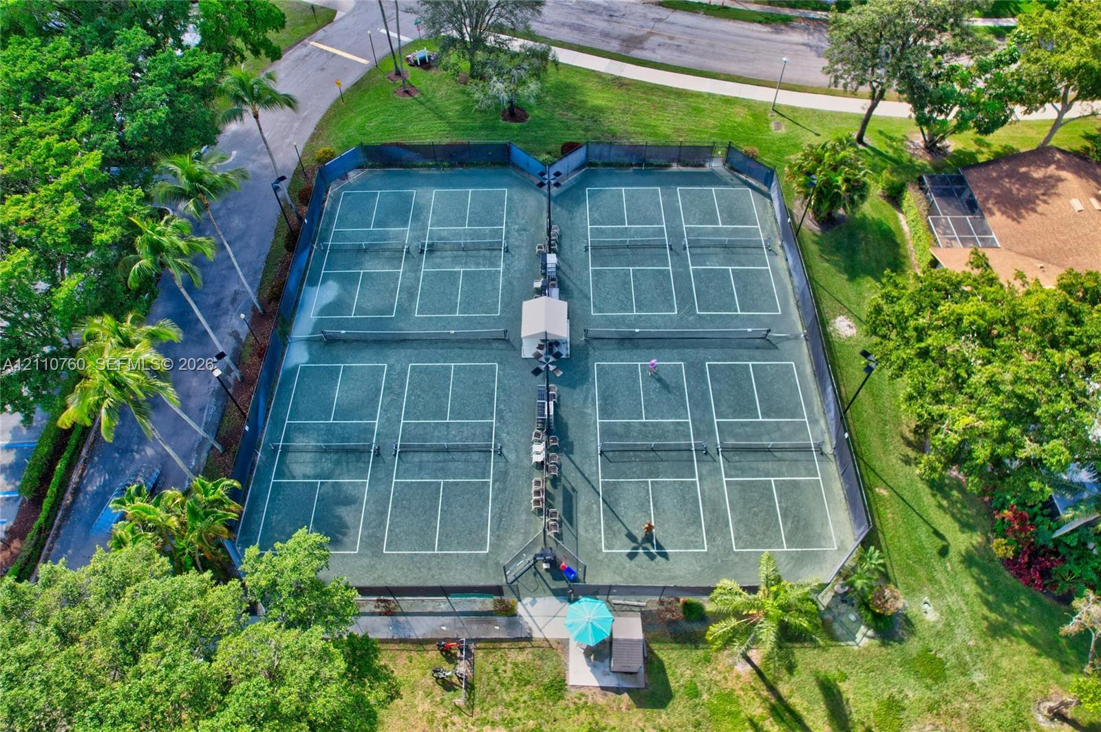 Four professional pickleball courts featuring specialized surfacing, perimeter chain-link fencing, stadium-style lighting, and mature perimeter landscaping