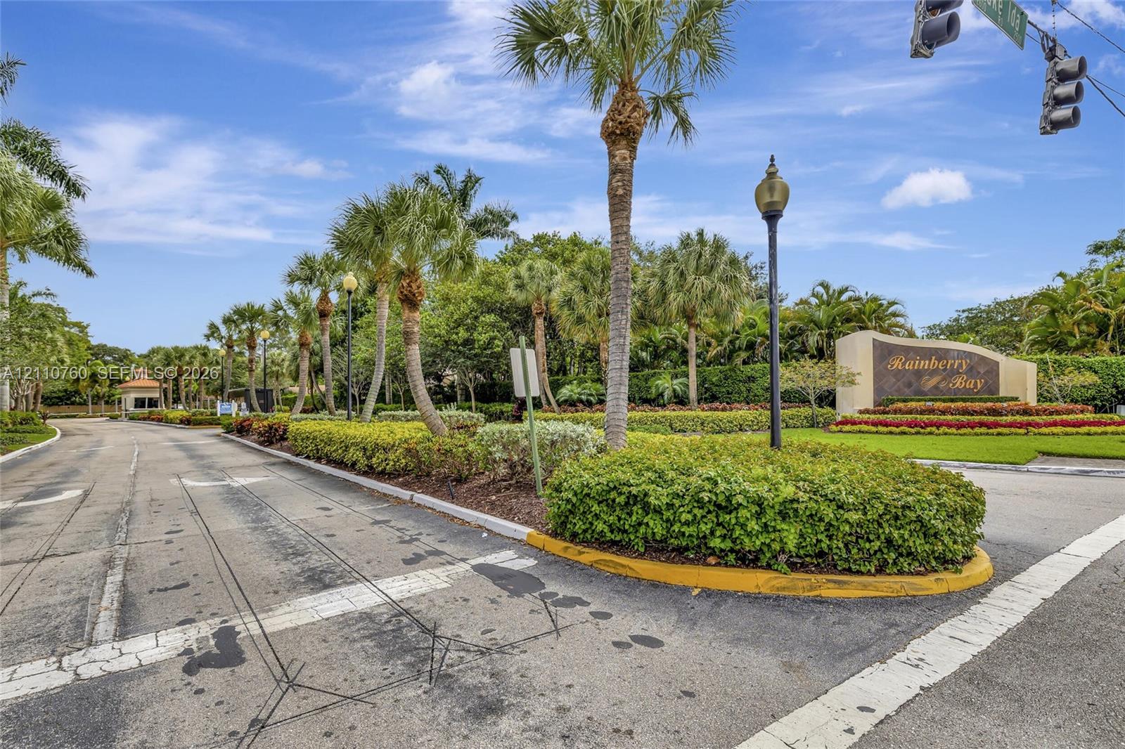 Community entrance featuring a monument sign, mature palm trees, professional landscaping, and ornamental street lighting