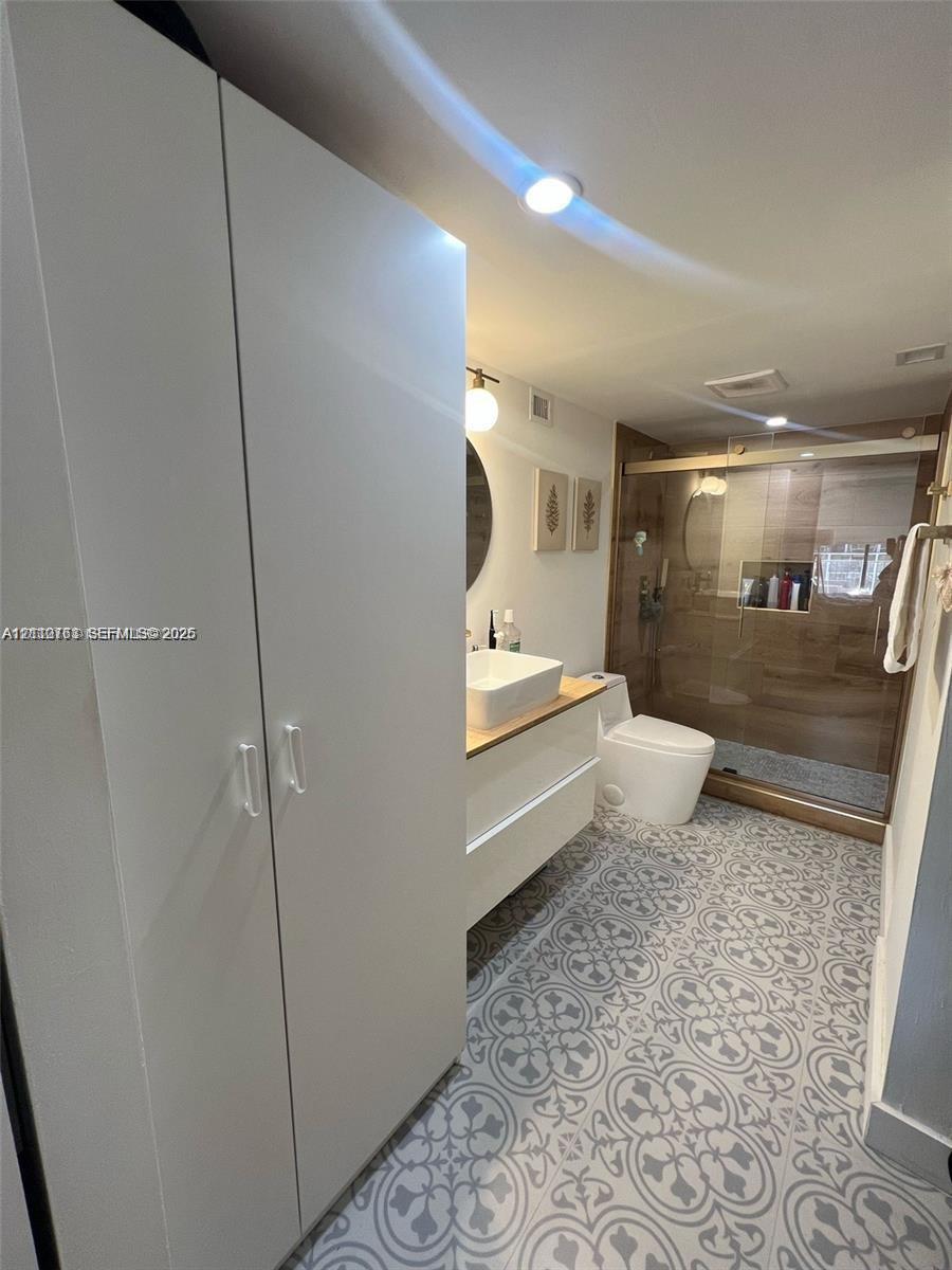 Bathroom featuring a white floating vanity with a vessel sink, patterned tile flooring, built-in floor-to-ceiling cabinetry, and a walk-in shower with glass enclosure Bathroom featuring a white floating vanity with a vessel sink, patterned tile flooring, built-in floor-to-ceiling cabinetry, and a walk-in shower with glass enclosure