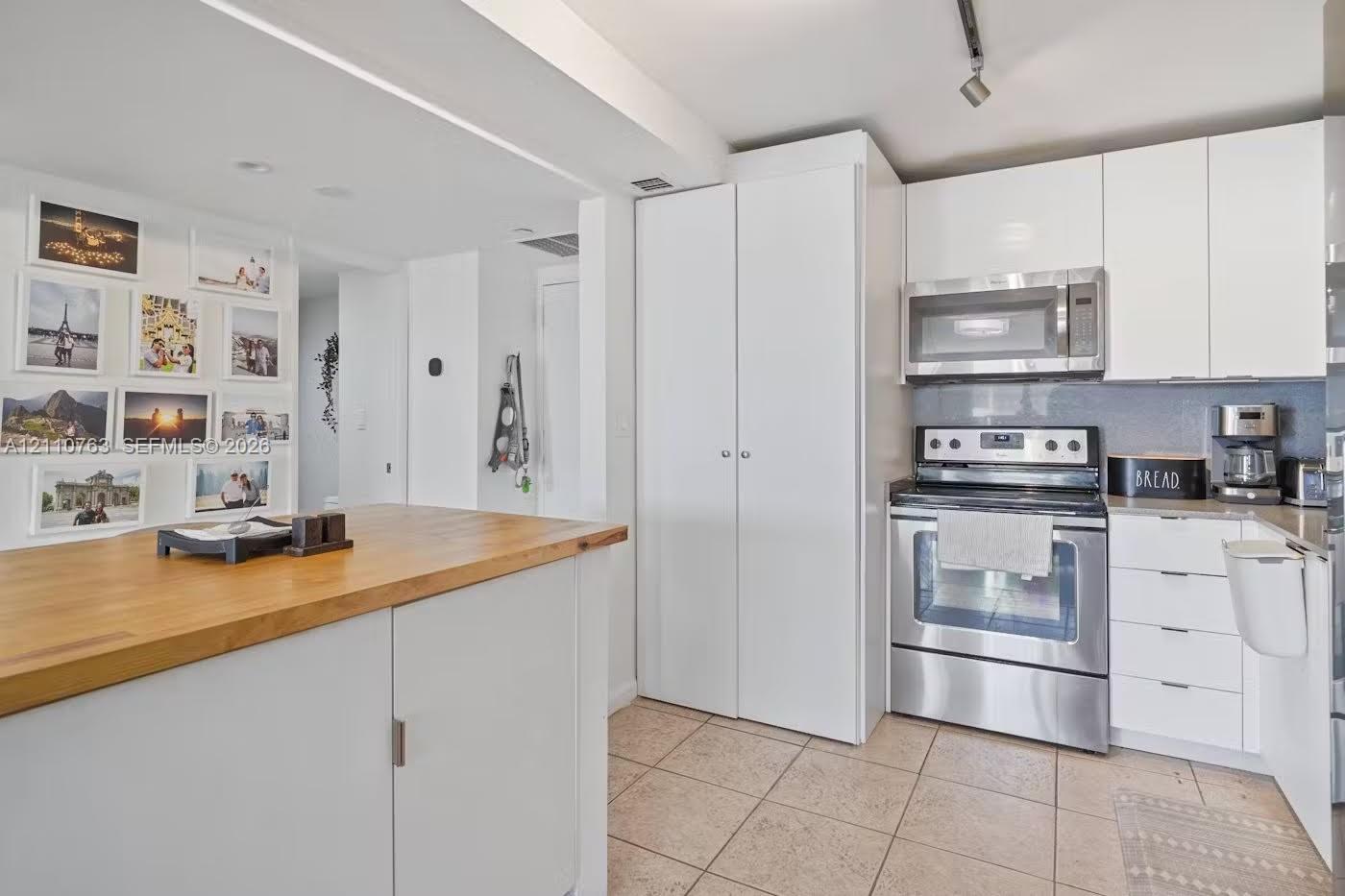 Kitchen featuring white flat-panel cabinetry, stainless steel appliances, a butcher block-topped island, and tile flooring Kitchen featuring white flat-panel cabinetry, stainless steel appliances, a butcher block-topped island, and tile flooring