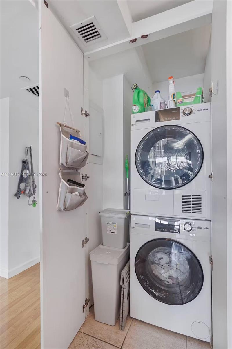 Dedicated laundry closet featuring a stacked front-loading washer and dryer set with tile flooring