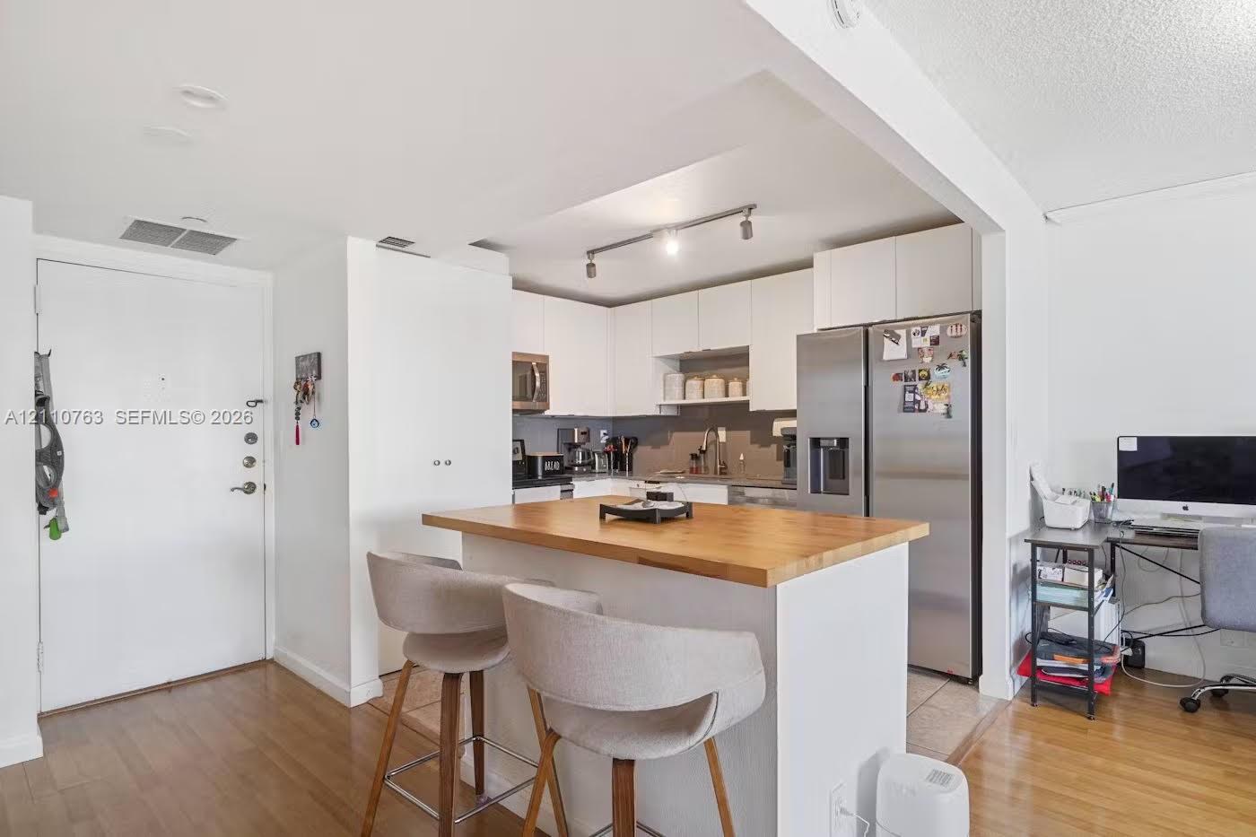 Kitchen featuring white cabinetry, wood-finish flooring, a central island with a wood countertop, stainless steel refrigerator, and recessed track lighting Kitchen featuring white cabinetry, wood-finish flooring, a central island with a wood countertop, stainless steel refrigerator, and recessed track lighting