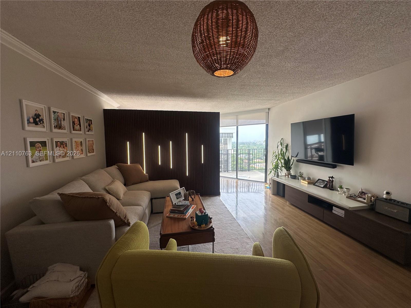 Living area featuring wood-finish flooring, a decorative vertical slat room divider with integrated linear lighting, a woven drum pendant light, and floor-to-ceiling glass sliding doors
