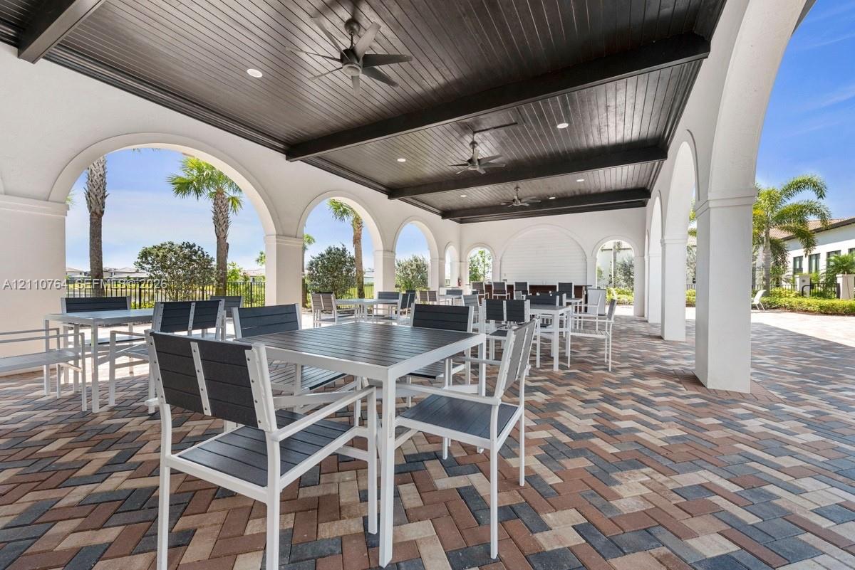 Covered outdoor loggia featuring architectural arched columns, dark wood-plank ceiling, recessed lighting, ceiling fans, and multi-tone herringbone paver flooring