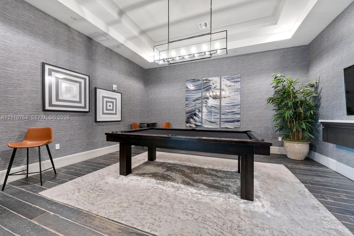 Textured grey wall covering, tray ceiling, rectangular linear pendant light fixture, and dark wood-finish tile flooring