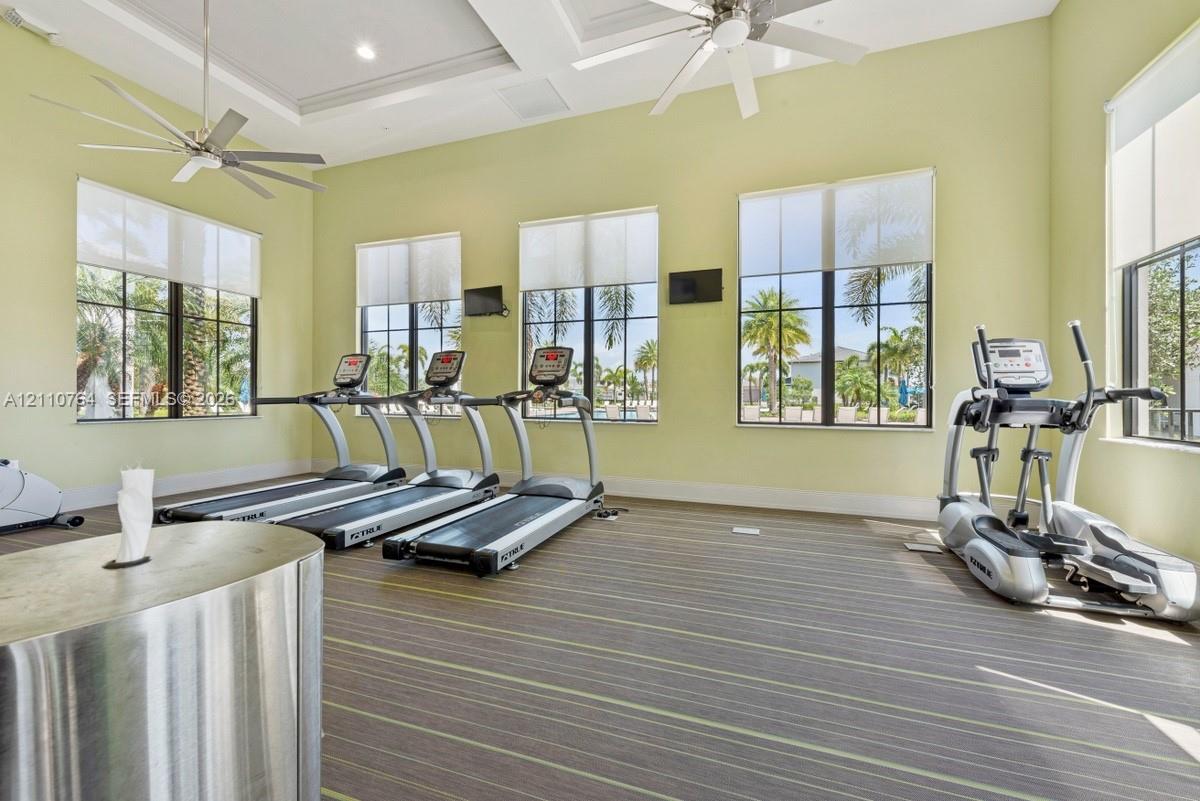 Fitness center featuring high ceilings with dual overhead fans, multi-pane windows with roller shades, and low-profile textured carpeting