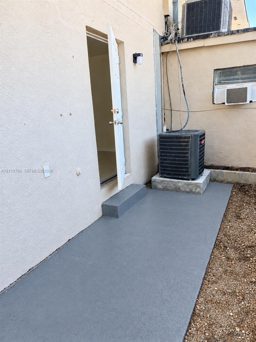 Stucco exterior featuring a dedicated concrete slab, single-step entry, and wall-mounted exterior lighting