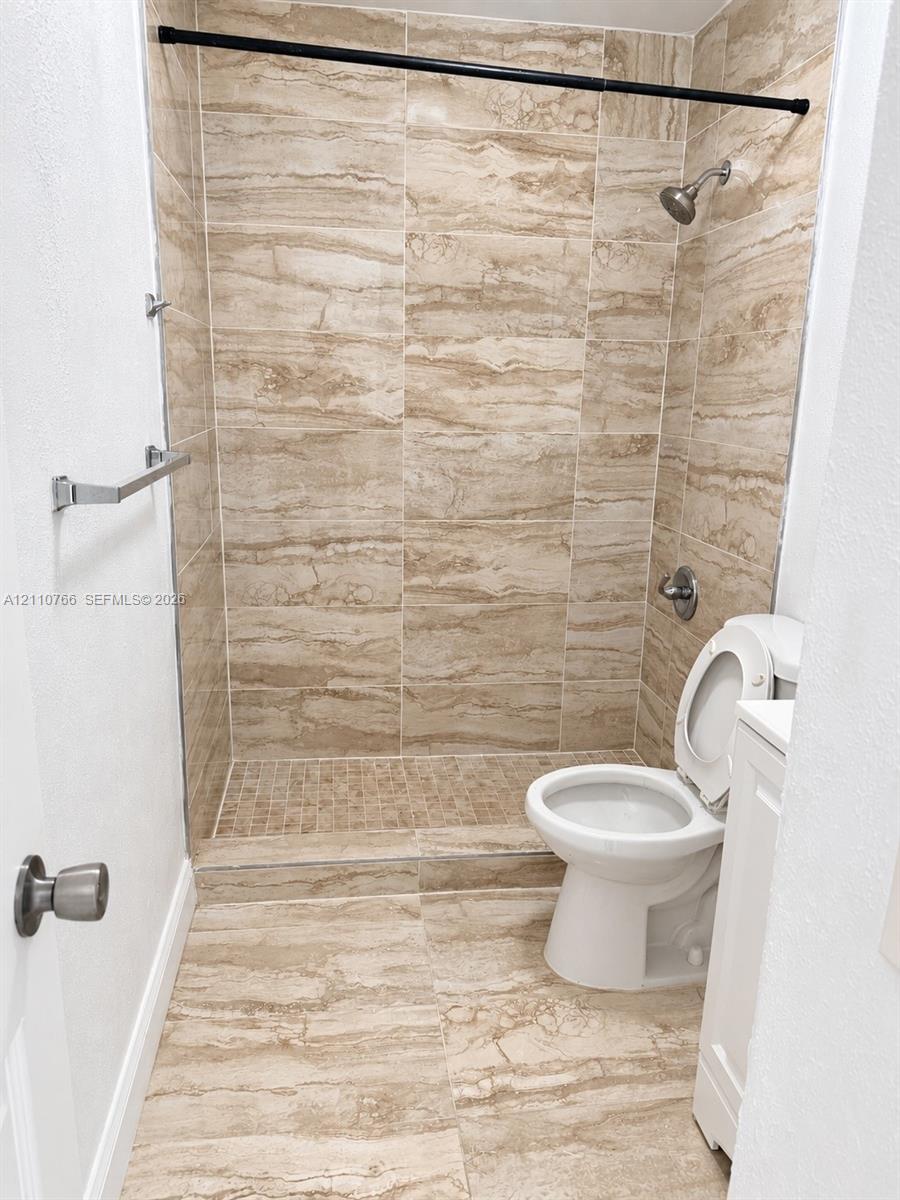 Full-height neutral-toned tile shower surround with matching floor tile, walk-in shower stall with mosaic tiled base, and wall-mounted metallic fixtures