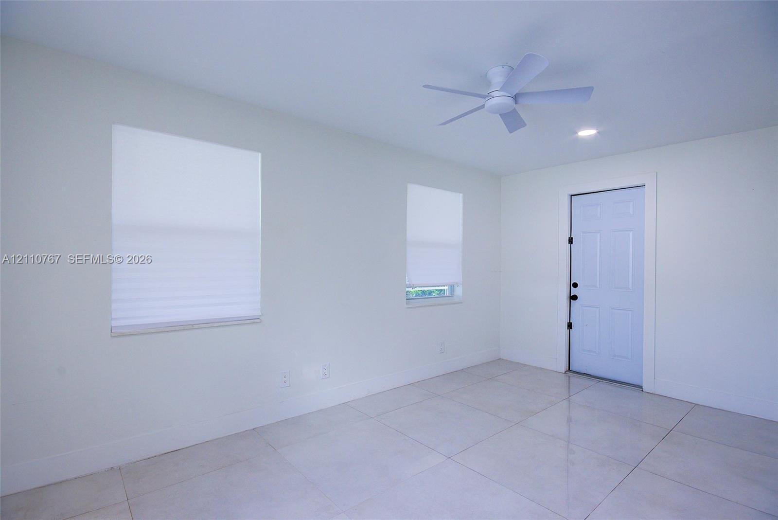 Light-filled room featuring neutral tile flooring, a six-panel exterior door, a multi-blade ceiling fan, and recessed lighting