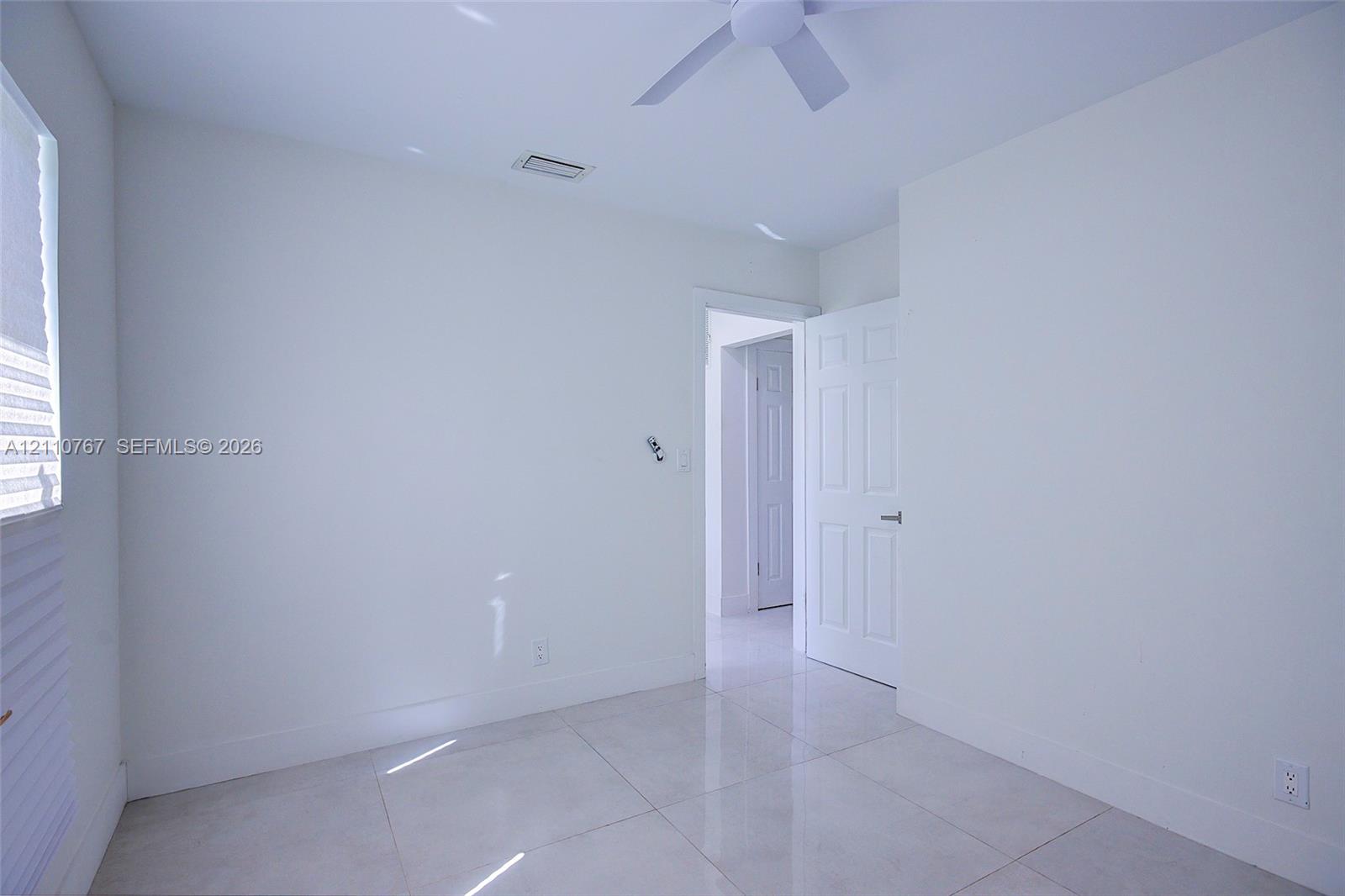 Interior room featuring large-format tile flooring, a neutral white color palette, and a white ceiling fan with integrated lighting