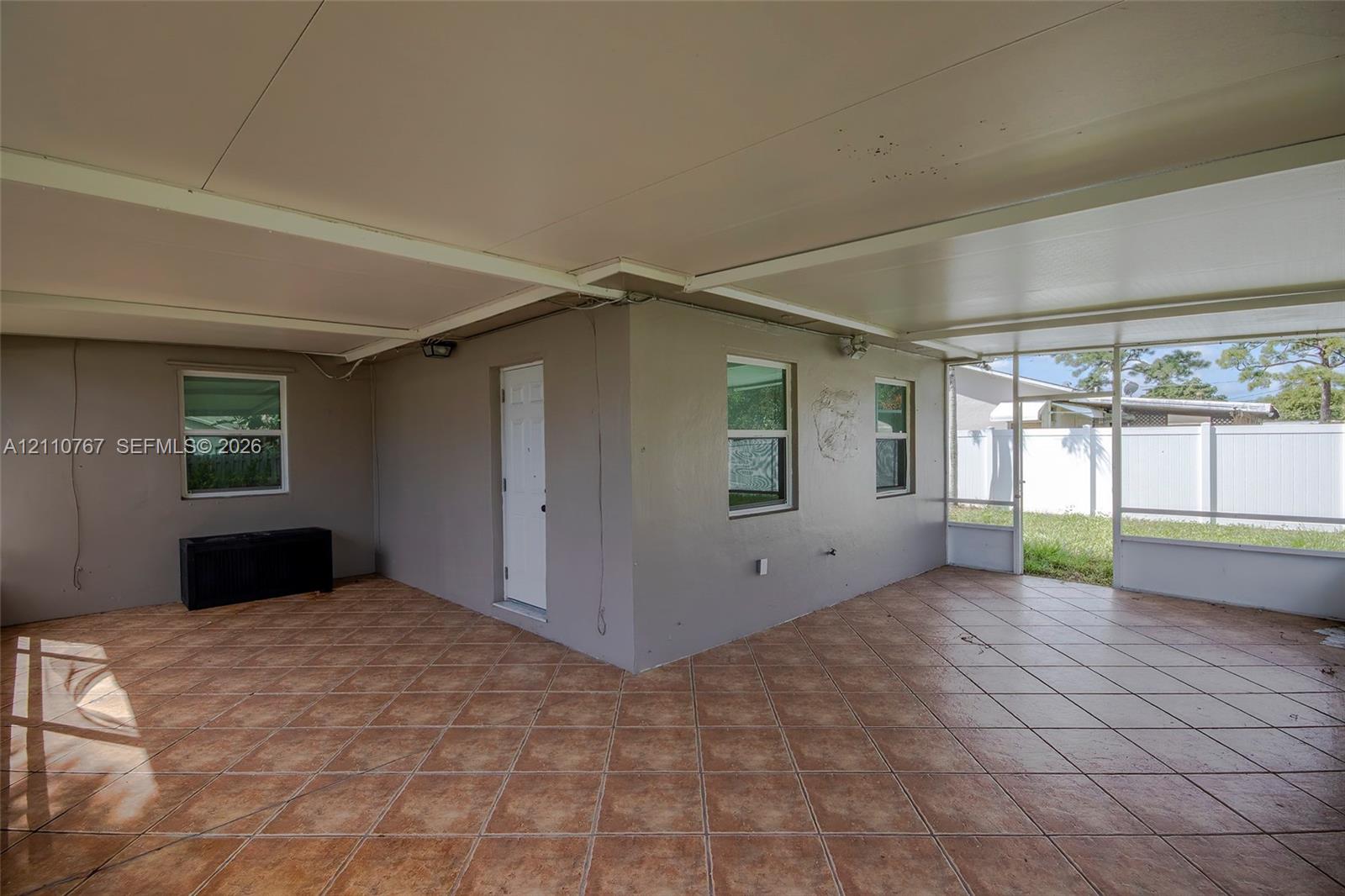 Covered patio featuring ceramic tile flooring, solid wall construction, white exterior door, and screen-enclosed sections