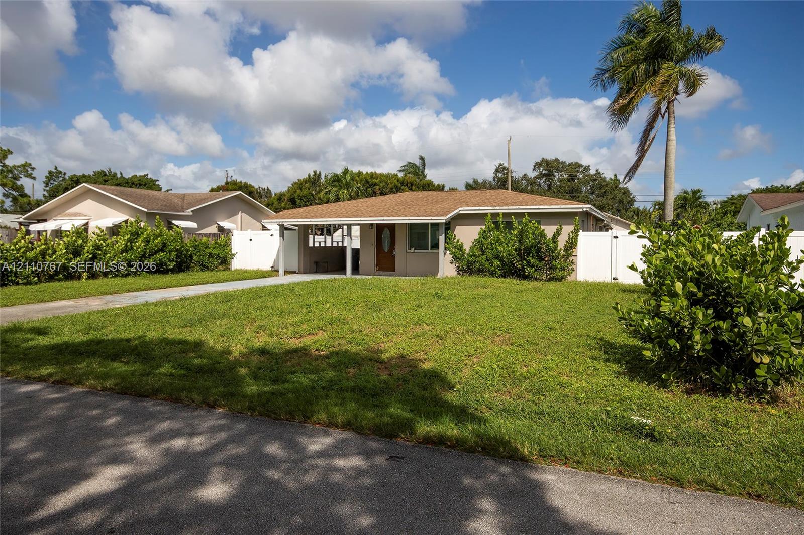 Single-story residence featuring a covered front entryway, shingled roof, stucco exterior, paved driveway, and perimeter white vinyl fencing