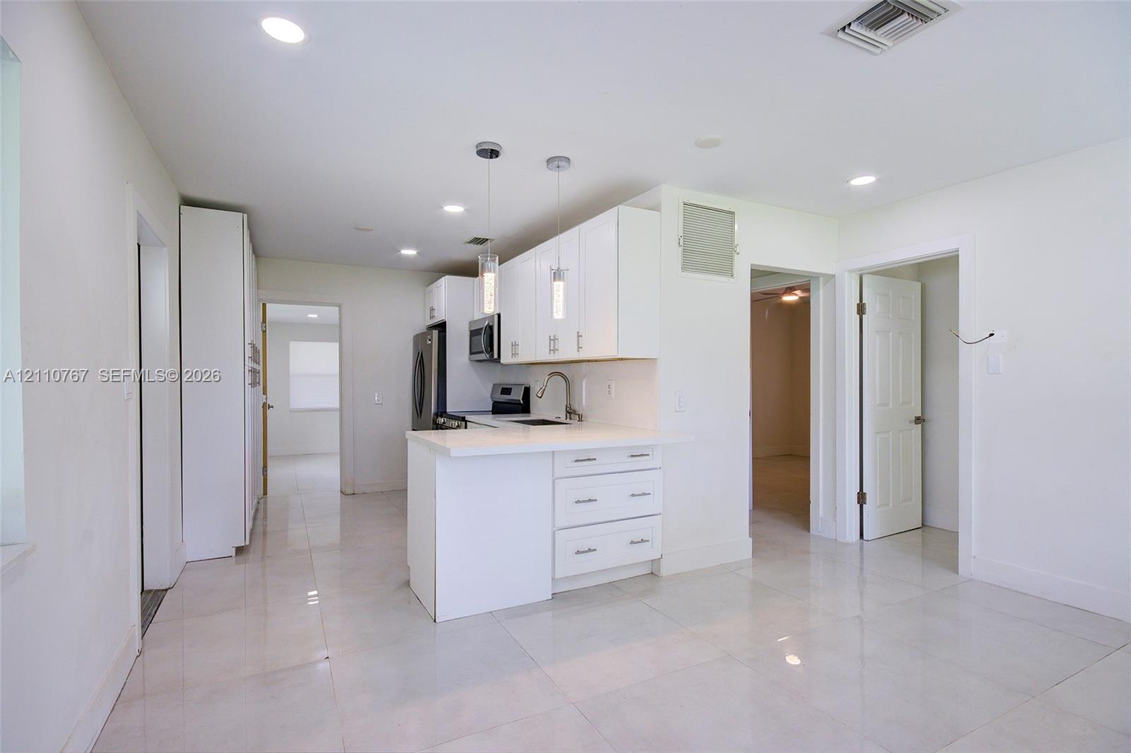 Kitchen featuring white shaker-style cabinetry, solid-surface countertops, dual pendant lighting, stainless steel appliances, and tile flooring