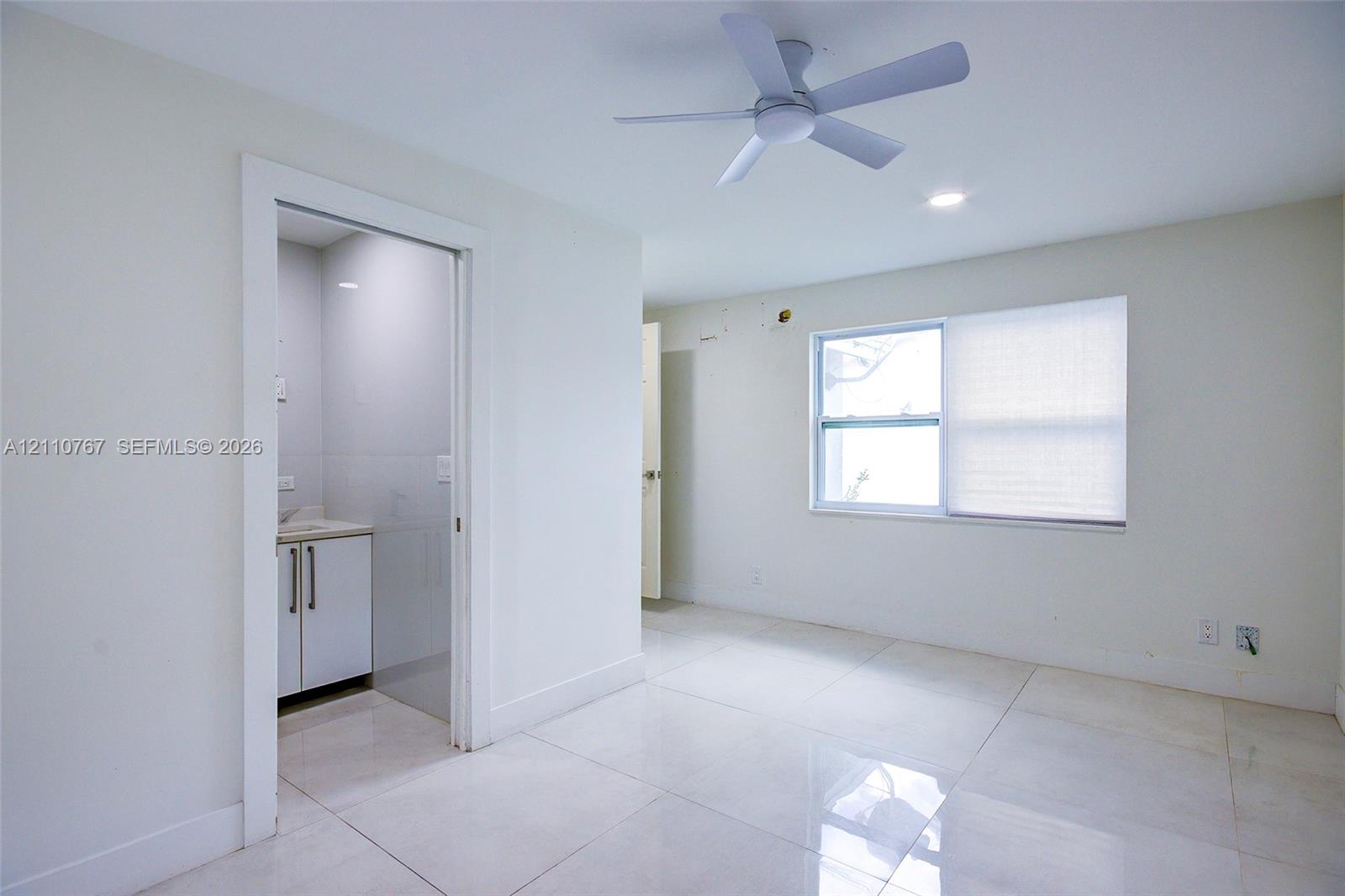 Interior space featuring white tile flooring, recessed ceiling lighting, a three-blade ceiling fan, and a single-hung window with shades