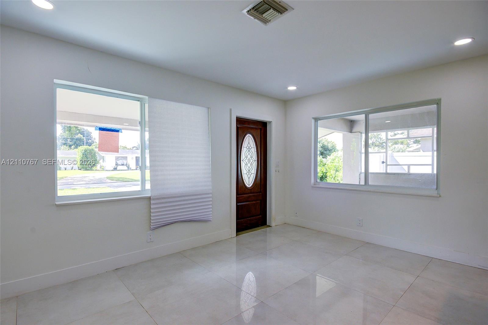Interior space featuring large-format tile flooring, recessed ceiling lighting, two expansive windows, and a wood-finish entry door with an oval glass insert