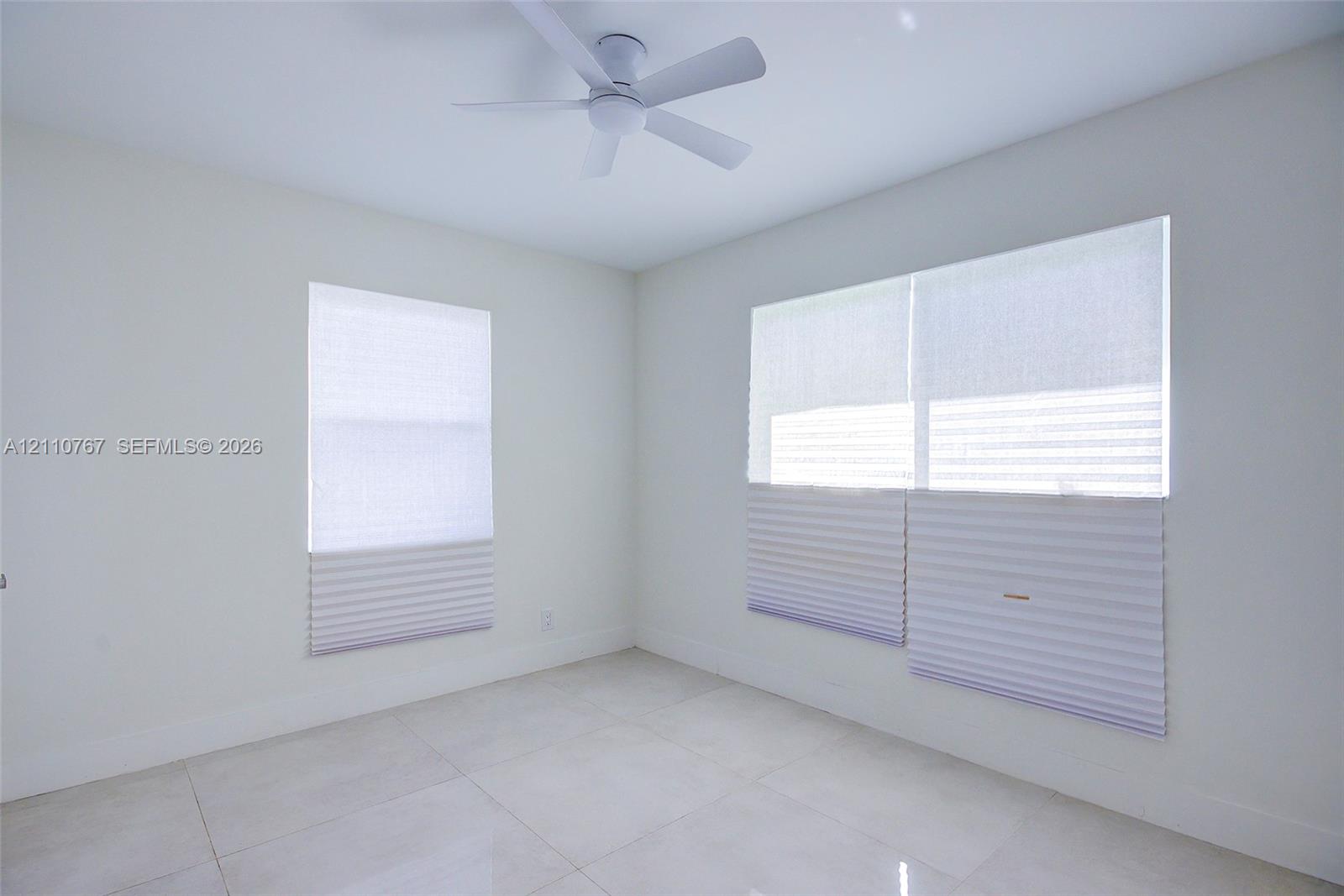 Neutral-toned room featuring large-format tile flooring, a contemporary ceiling fan, and dual windows equipped with cordless pleated shades