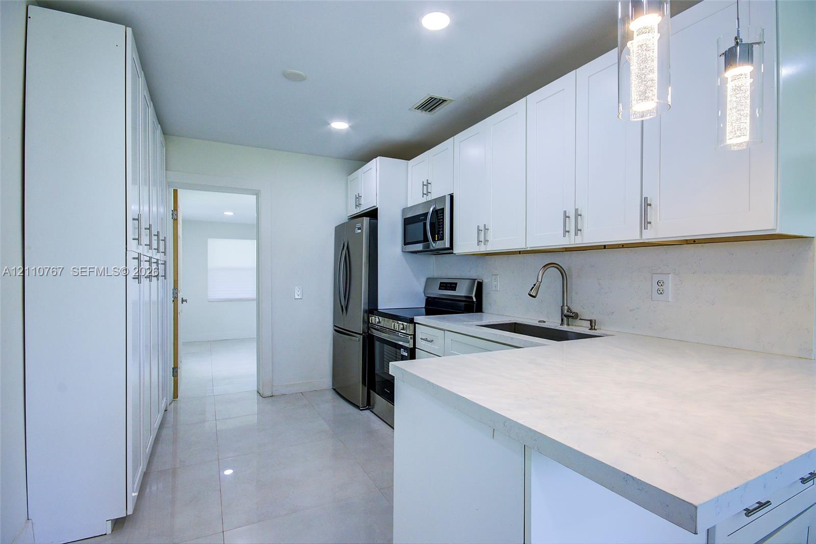 Kitchen featuring white shaker cabinetry, stone-finish countertops, stainless steel appliances, tile flooring, and glass pendant lighting