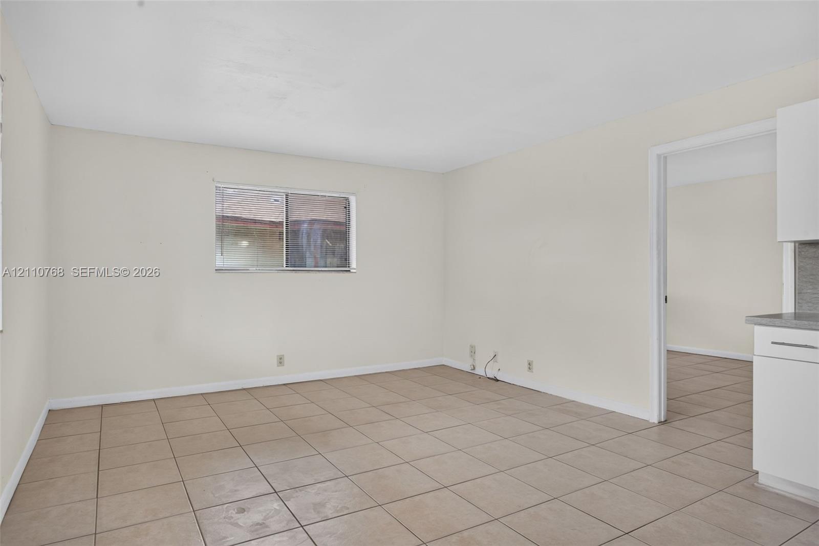 Neutral-toned interior space featuring light-colored wall finishes, ceramic tile flooring, and a sliding glass window