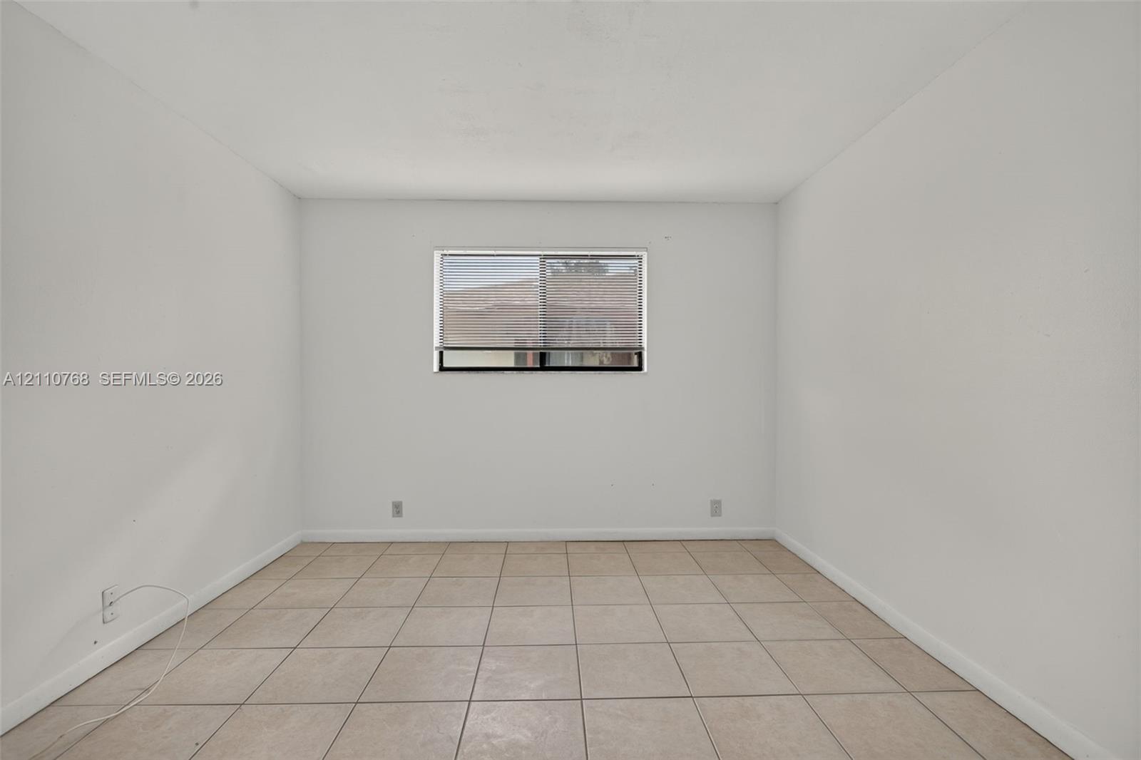 Neutral interior space featuring light-toned floor tile and a central window with horizontal blinds