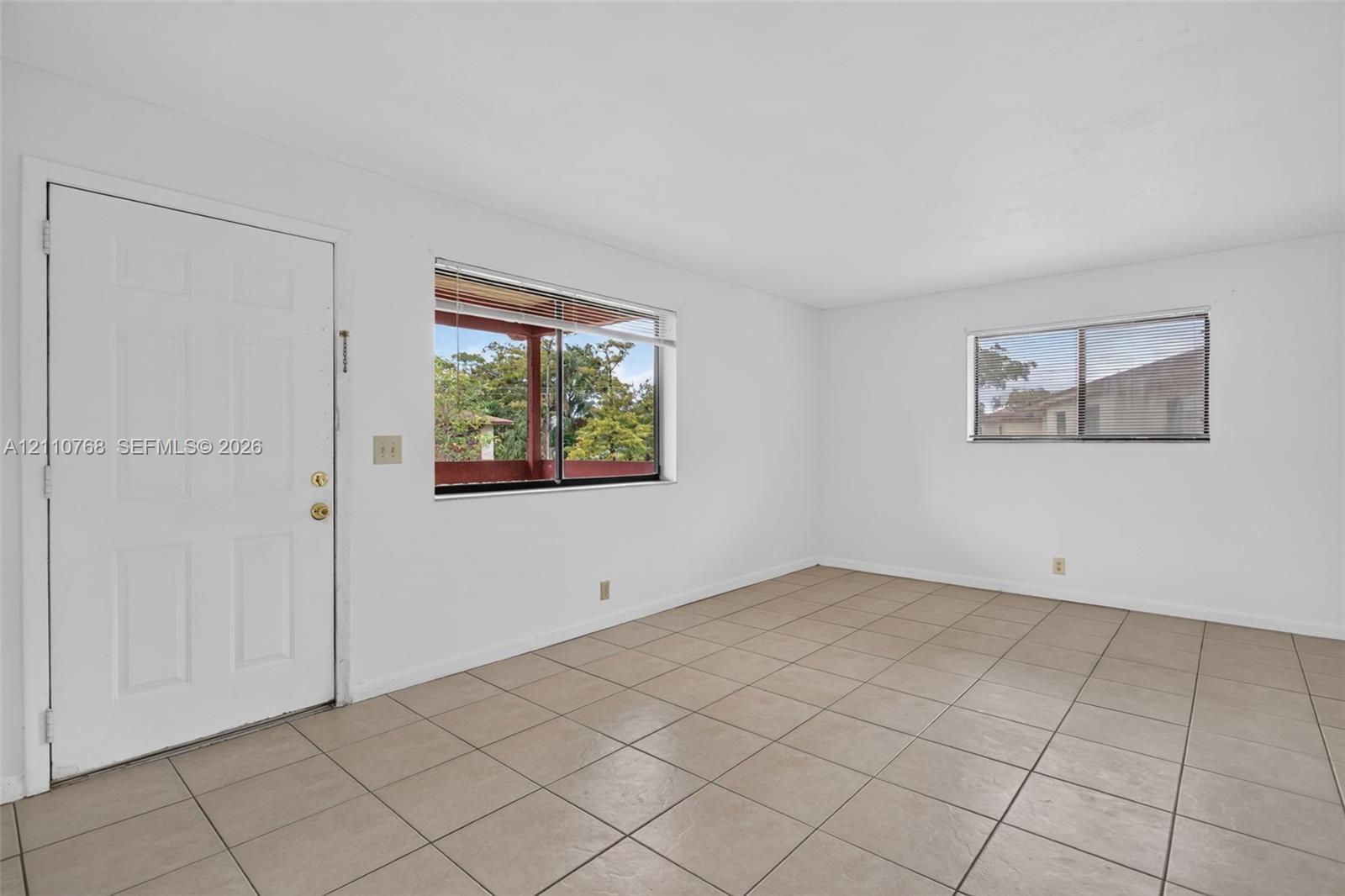 Neutral-toned square tile flooring, white wall surfaces, and two windows with horizontal blinds