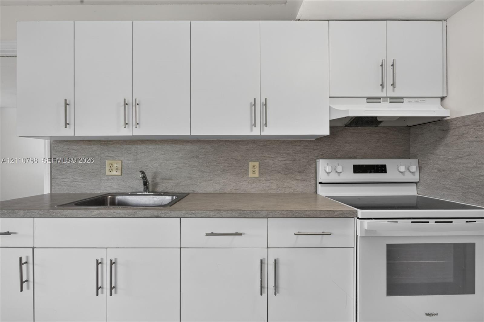 Kitchen featuring white flat-panel cabinetry, neutral stone-finish countertops, stainless steel sink with a metallic faucet, and a white electric range with a built-in range hood