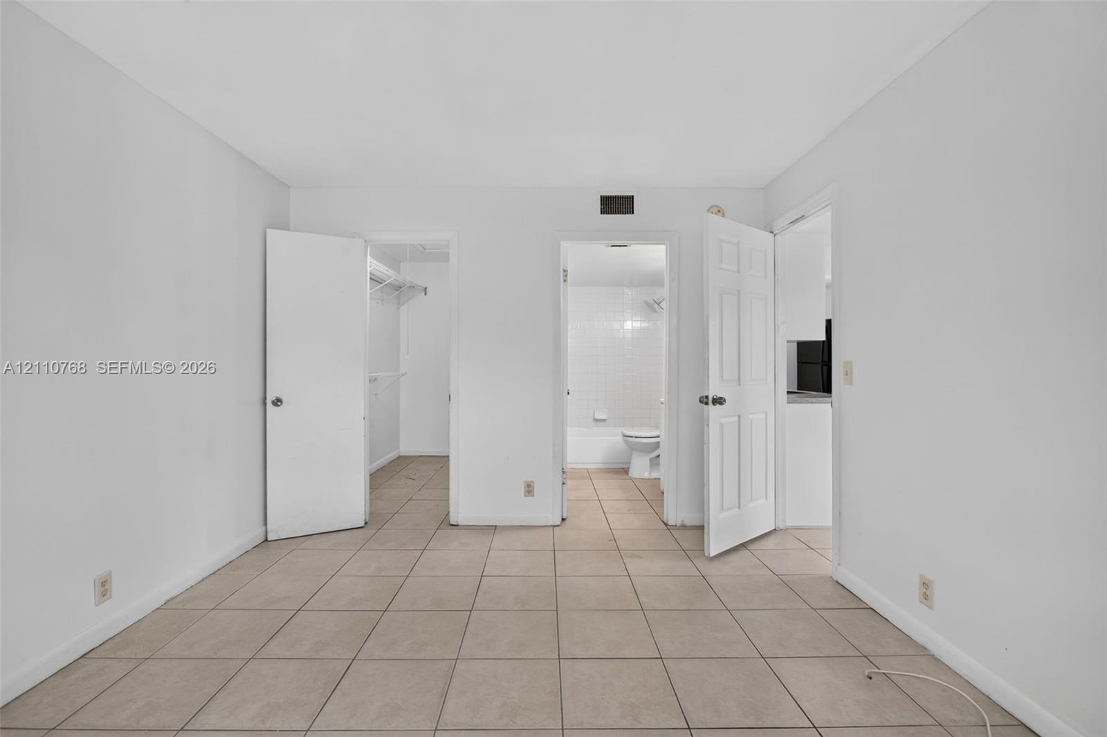 Room interior featuring neutral ceramic tile flooring, two paneled doors, and direct entry points to a walk-in closet and a tiled bathroom
