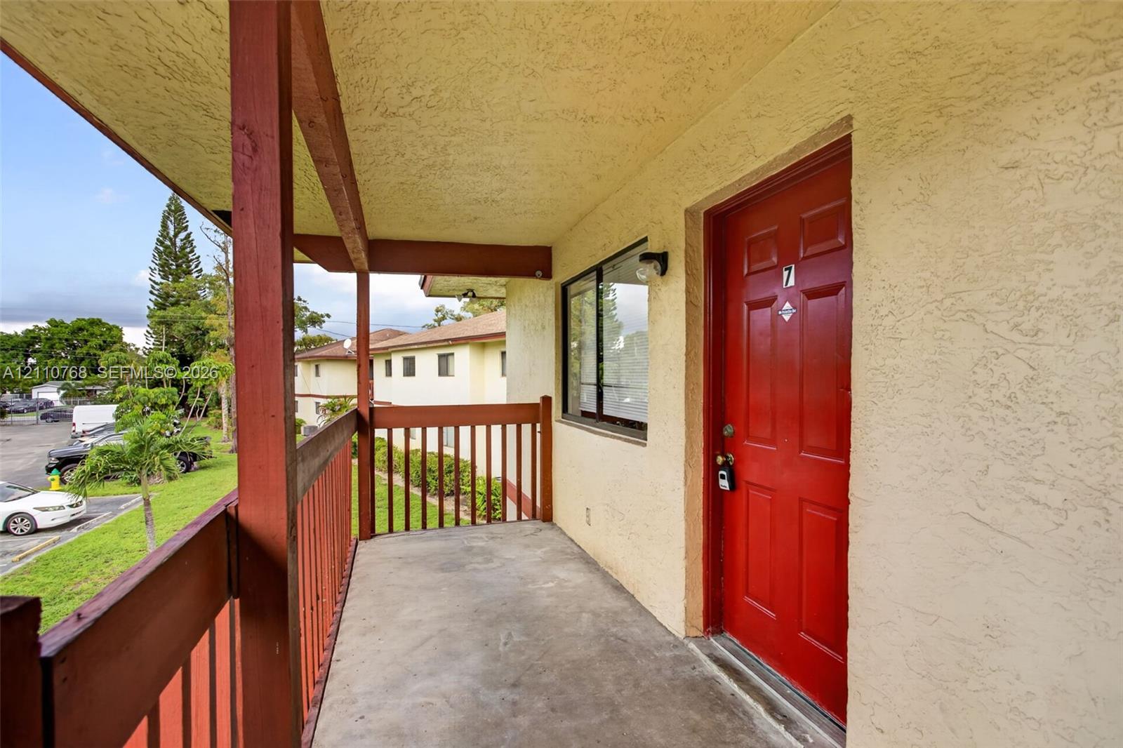 Covered exterior walkway featuring concrete flooring, a paneled door, and wood-style railing