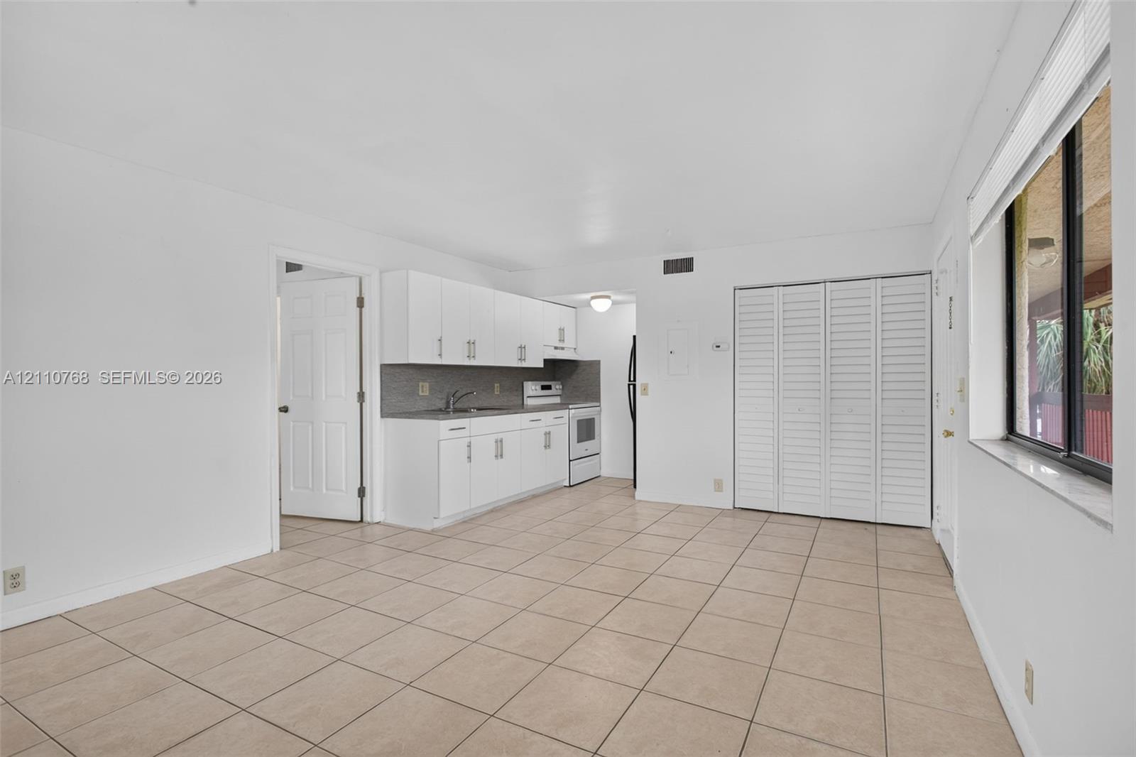 Kitchen featuring white cabinetry, solid-surface countertops, tile backsplash, and tile flooring, including a built-in louvered-door closet