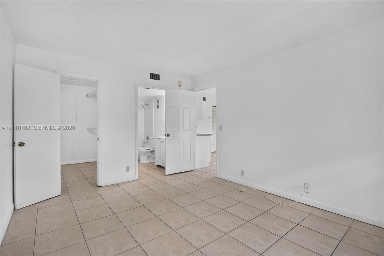 Neutral-toned ceramic tile flooring, walk-in closet with built-in wire shelving, and solid-core interior doors