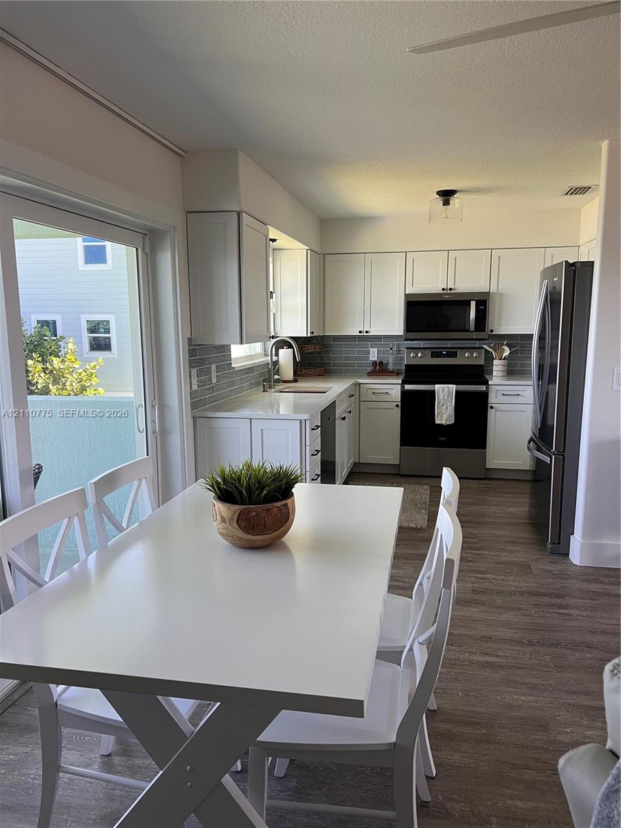 Kitchen featuring white cabinetry, solid-surface countertops, subway tile backsplash, stainless steel appliances, and wood-finish flooring Kitchen featuring white cabinetry, solid-surface countertops, subway tile backsplash, stainless steel appliances, and wood-finish flooring