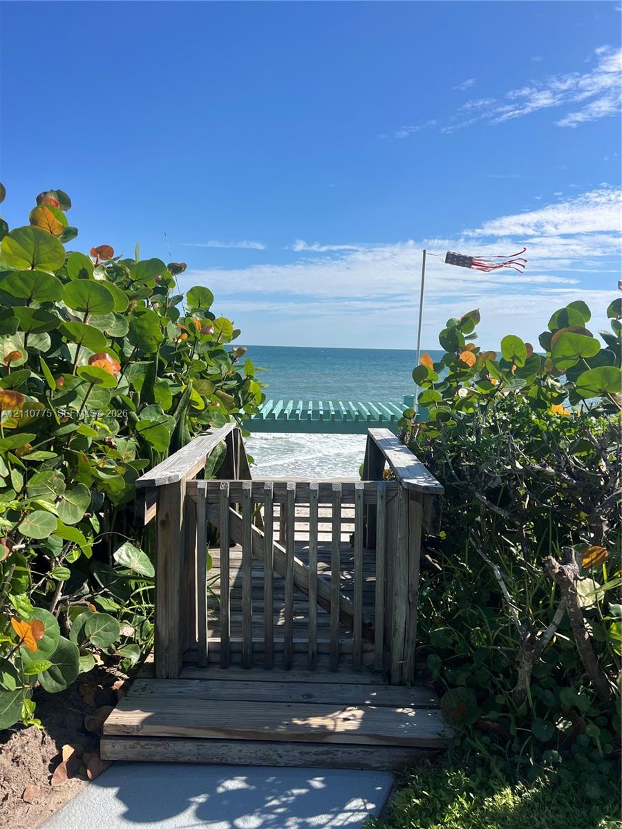 Private wooden beach access gate with a path leading to a timber pergola overlooking the ocean