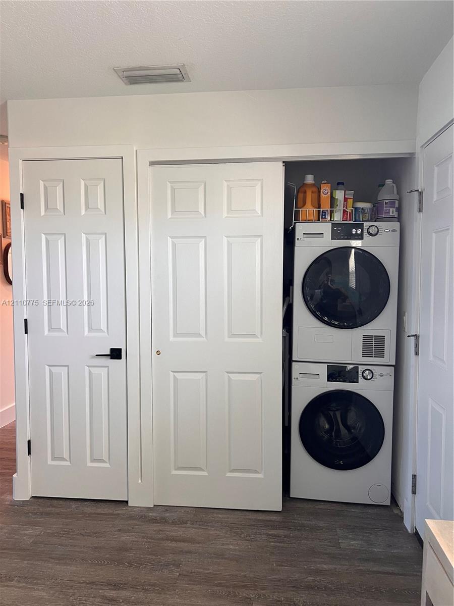 Laundry closet featuring stacked high-efficiency appliances, white paneled interior doors, matte black hardware, and wood-finish flooring