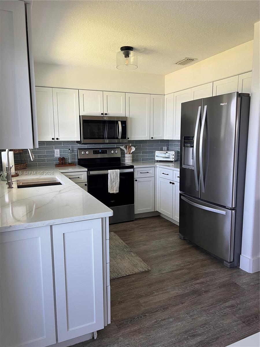 Kitchen featuring white shaker-style cabinetry, quartz countertops, subway tile backsplash, stainless steel appliances, and wood-finish flooring Kitchen featuring white shaker-style cabinetry, quartz countertops, subway tile backsplash, stainless steel appliances, and wood-finish flooring
