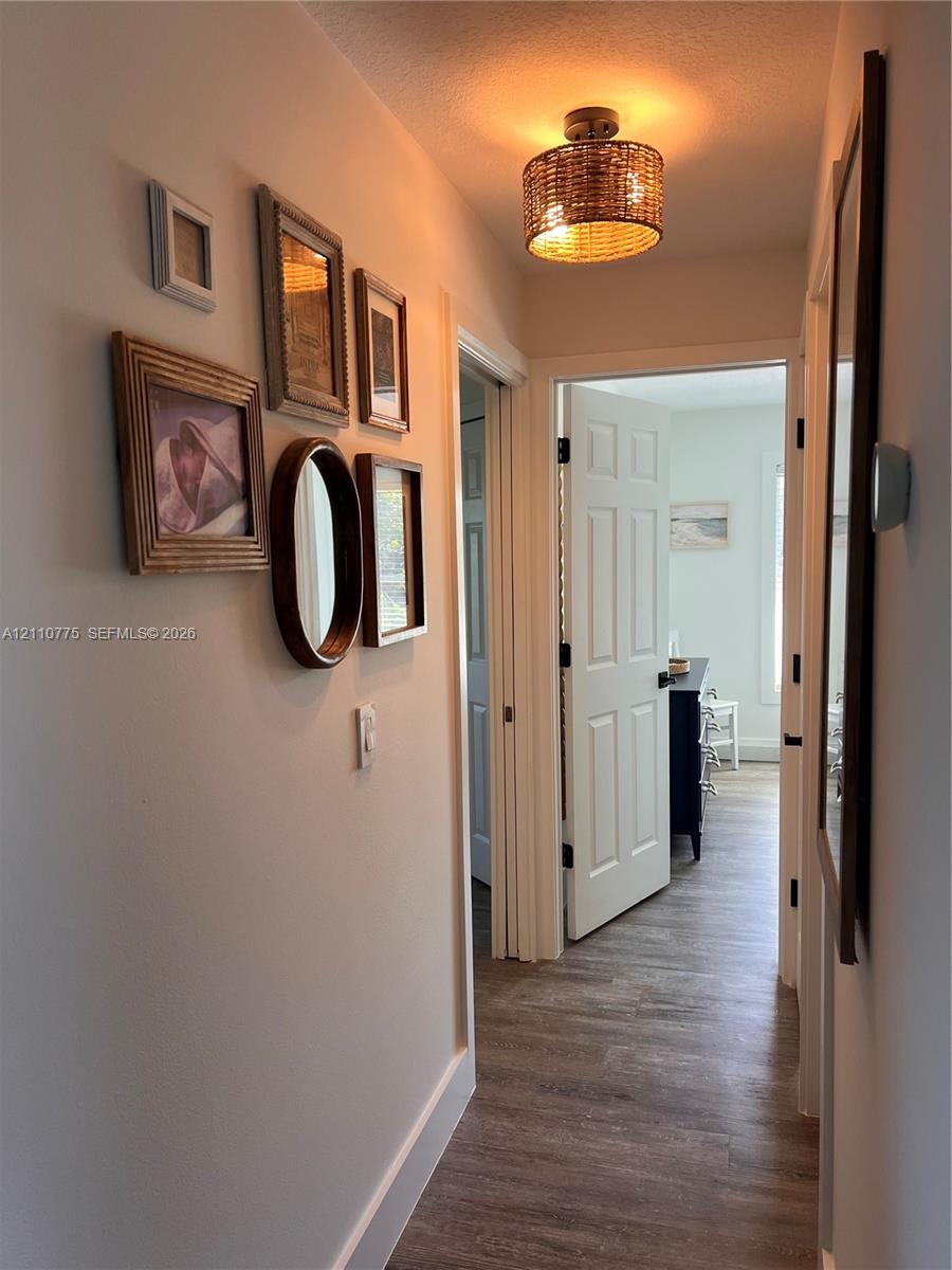 Hallway featuring wood-finish flooring, a woven drum flush-mount light fixture, and six-panel interior doors with matte black hardware